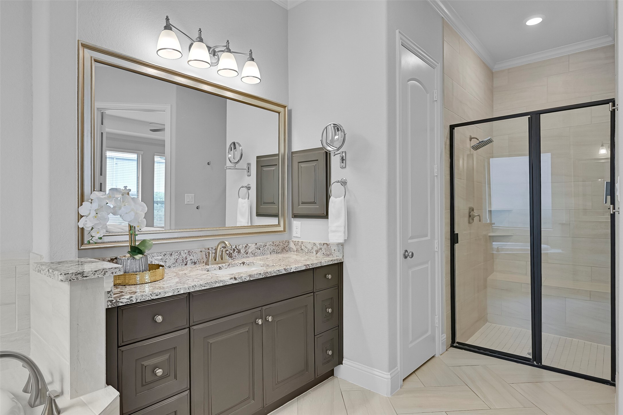 Another view highlights the oversized walk-in shower with tile surround, bench seating, and frameless-style glass enclosure. Separate vanities provide excellent storage and countertop space, while neutral finishes create a timeless and elegant design.