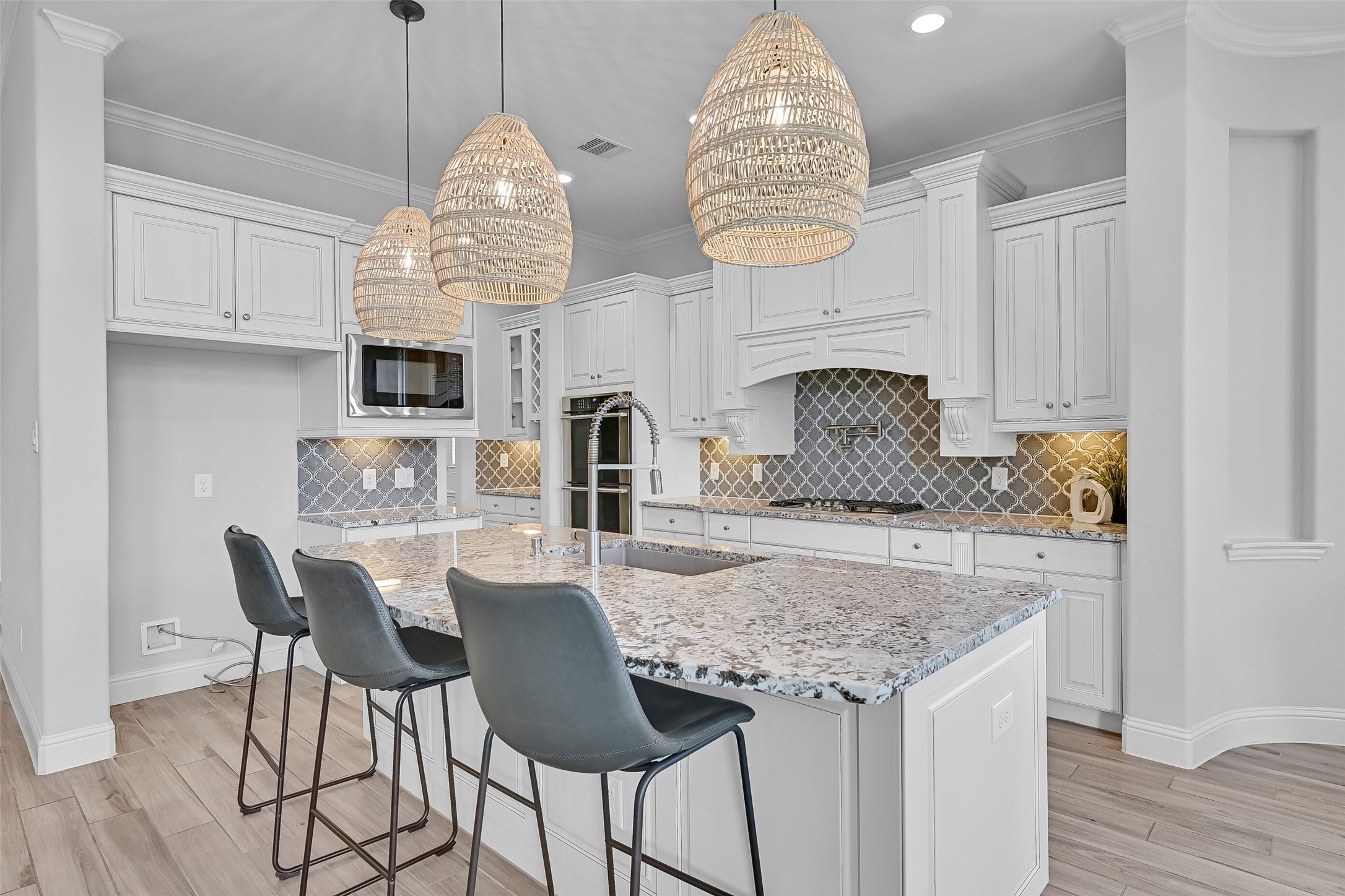 The island kitchen combines beauty and function with granite countertops, abundant cabinetry, undercabinet lighting, decorative crown molding, and stylish pendant lighting. A large curved island provides seating, prep space, and a central gathering point for family and guests.