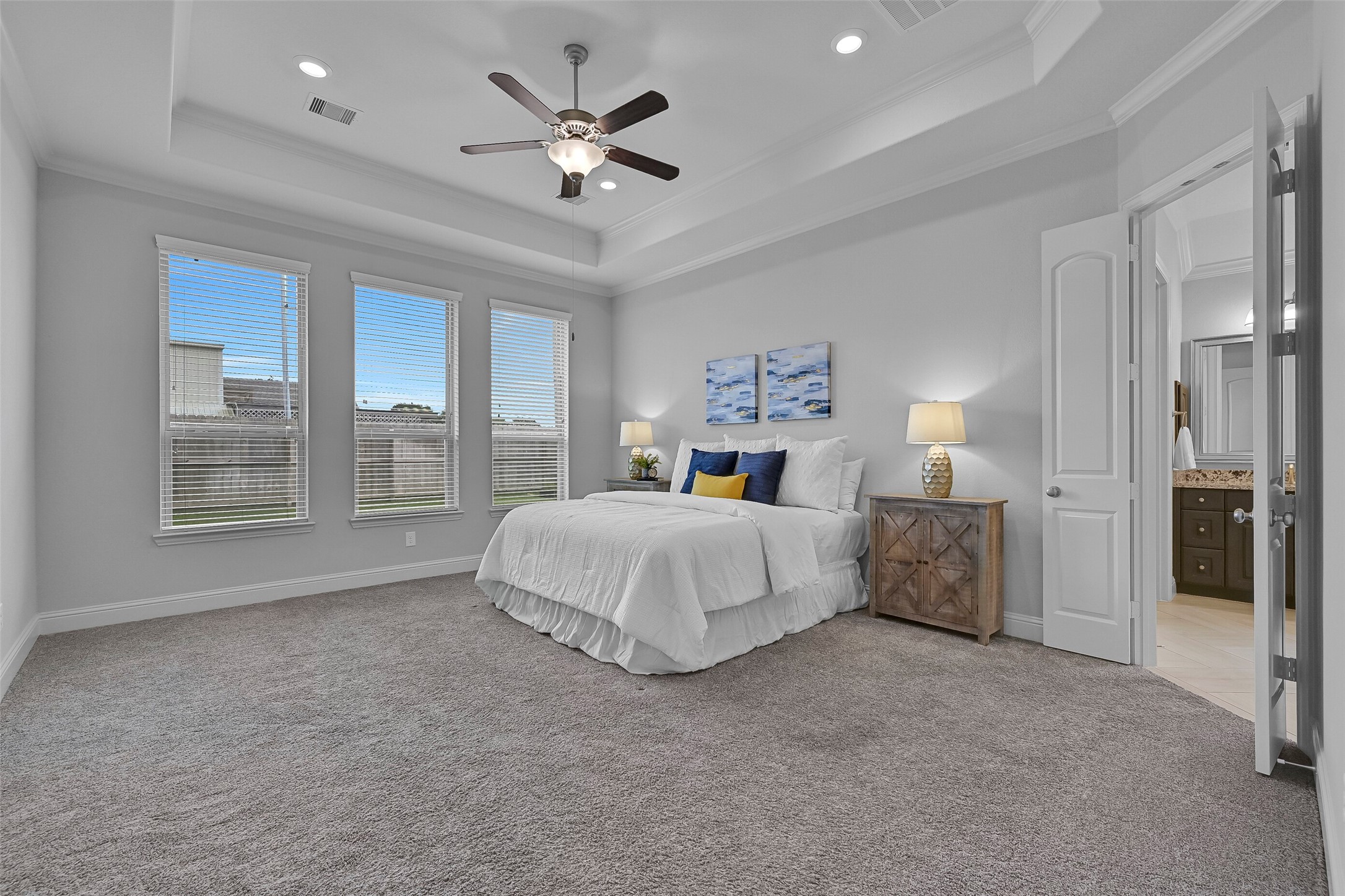 Tucked away at the rear of the home, the spacious primary suite offers an 11-foot tray ceiling trimmed with crown molding, recessed lighting, a lighted ceiling fan, plush carpet, and three large windows that fill the room with natural light while maintaining privacy.