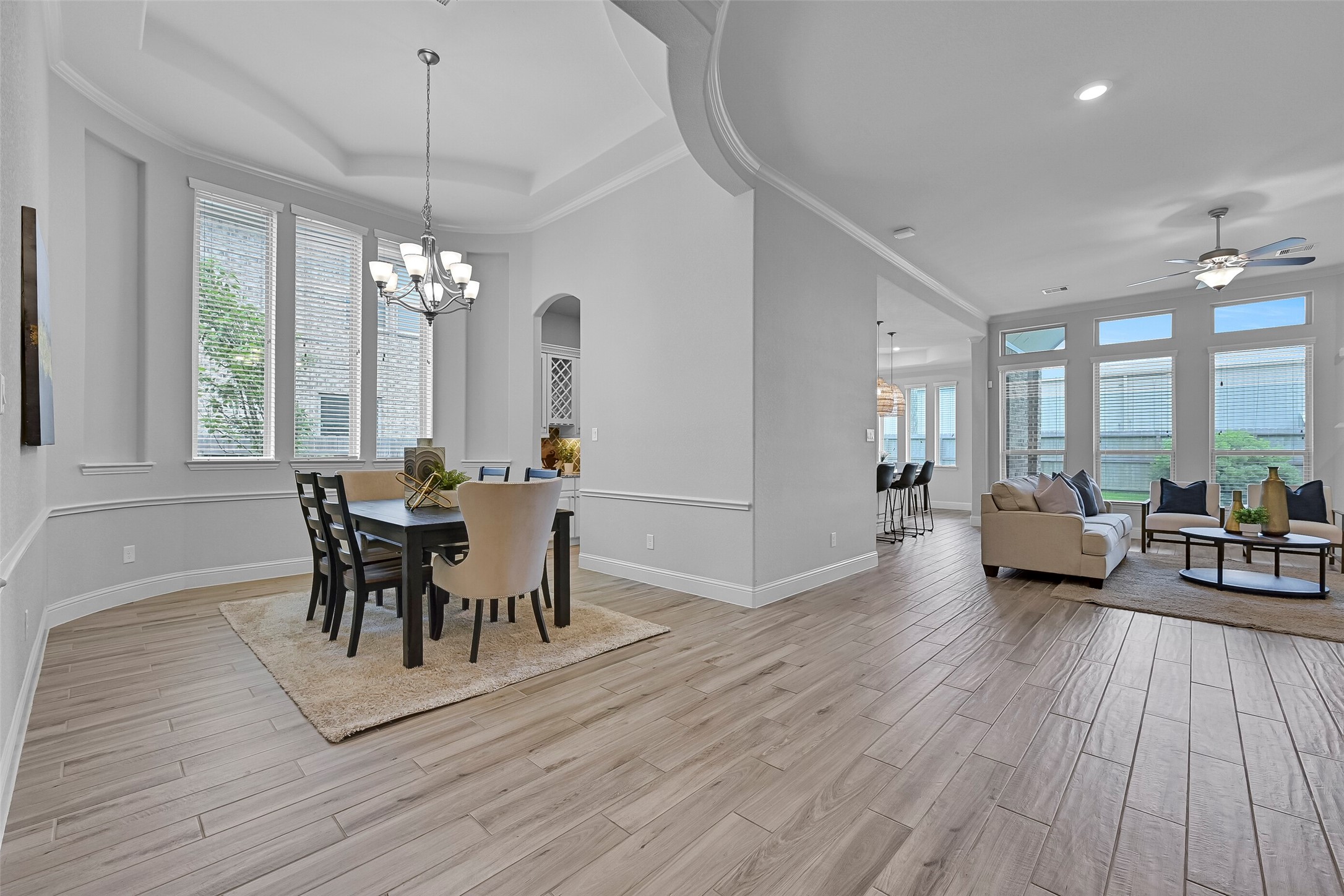 Looking beyond the dining room, you'll appreciate the openness of this Village Builders design. Wood-look tile flooring flows throughout the main living areas while walls of windows, soaring ceilings, and thoughtfully designed gathering spaces create a bright and connected feel throughout the first floor.