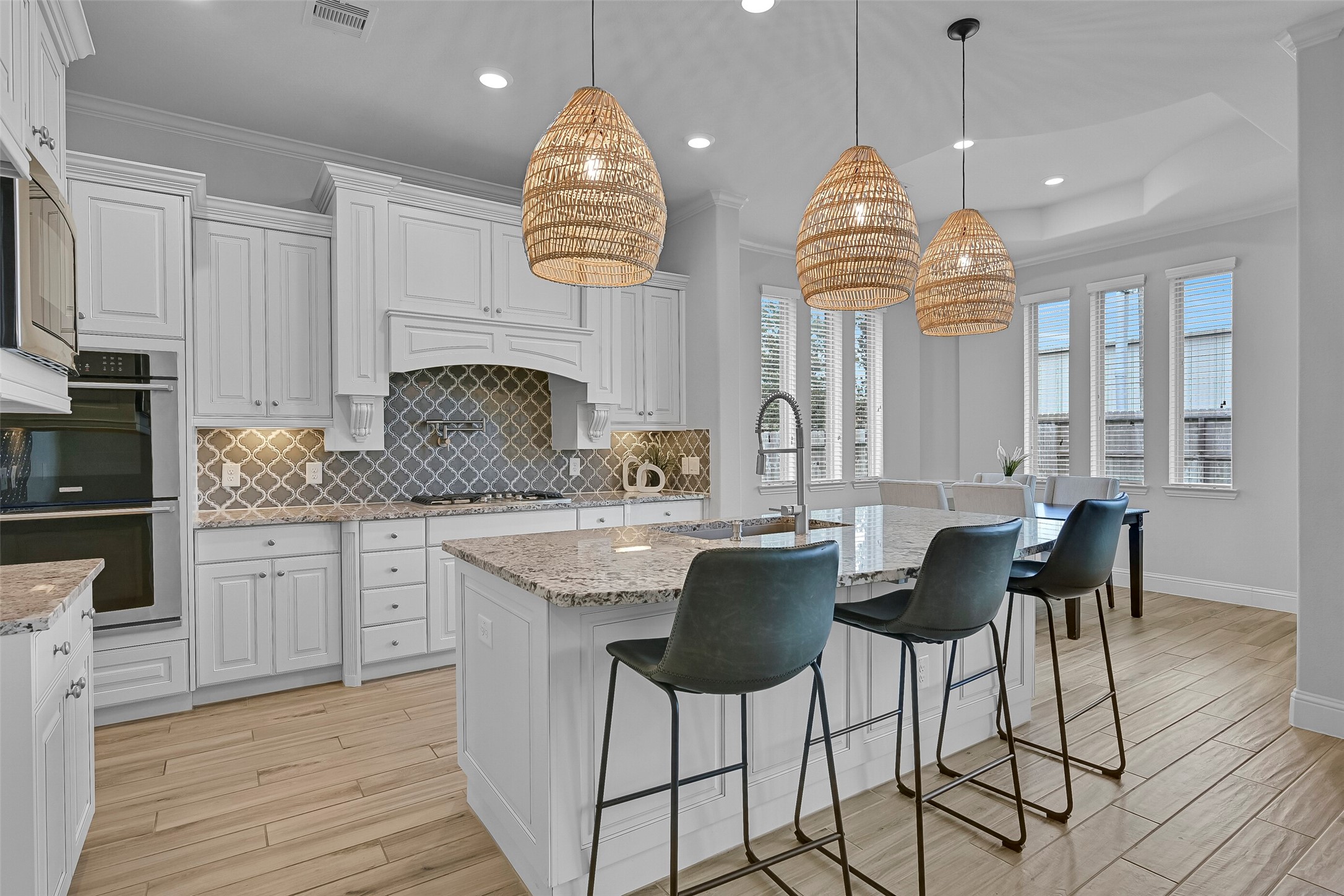 Designed for both everyday convenience and hosting guests, the island kitchen features granite countertops, an arabesque tile backsplash, undercabinet lighting, a 5-burner Electrolux gas cooktop with pot filler, dual Electrolux convection ovens, and a huge single-basin composite sink overlooking the breakfast room.