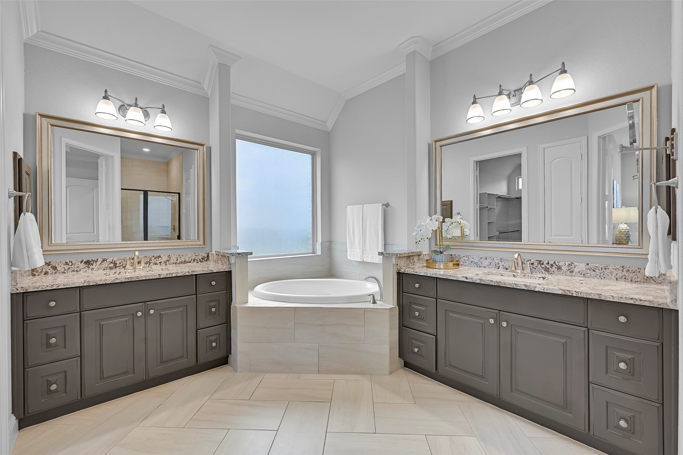 Step into the luxurious ensuite bath showcasing dual granite vanities, framed mirrors, upgraded cabinetry, a relaxing corner soaking tub, and abundant natural light. The thoughtful layout provides plenty of space for busy mornings while maintaining a spa-like feel.