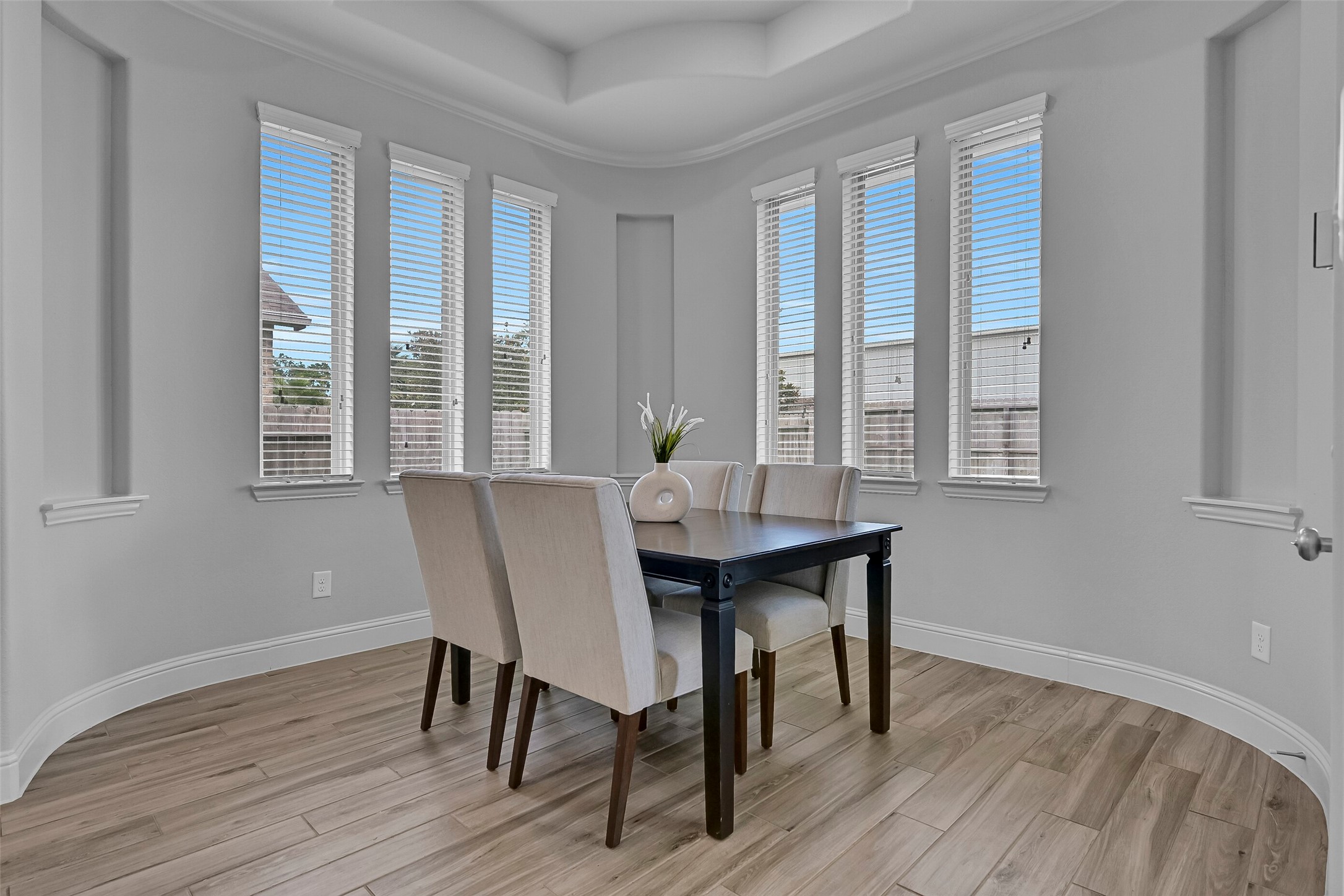 Surrounded by windows, the breakfast room features wood-look tile flooring, recessed lighting, and a tray ceiling overhead. Natural light pours into the space, creating a cheerful setting for morning coffee and casual meals while overlooking the backyard and covered patio.