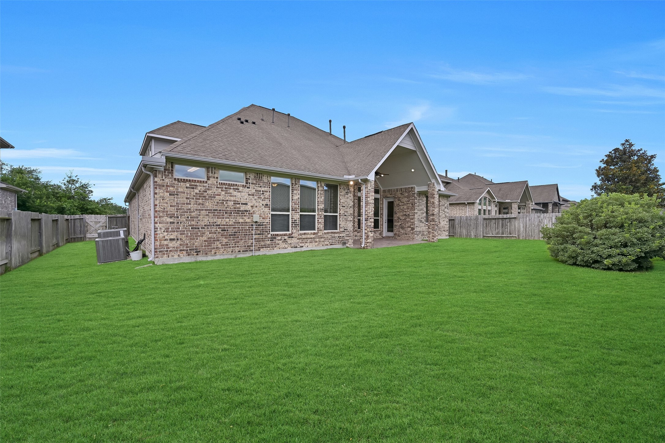 From this angle, the impressive depth and width of the backyard are fully appreciated. The expansive lawn provides room for pets, play equipment, or a custom pool while still leaving plenty of yard to enjoy. The home's attractive brick exterior, large windows, and covered patio create an inviting backdrop for outdoor living.