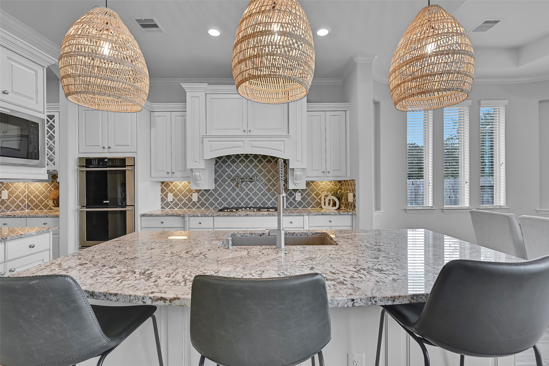 An oversized granite island anchors the kitchen and features a huge single-basin composite sink with a commercial-grade pull-down faucet. Beyond, you'll find custom cabinetry, dual Electrolux convection ovens, and a striking arabesque tile backsplash that extends throughout the space.