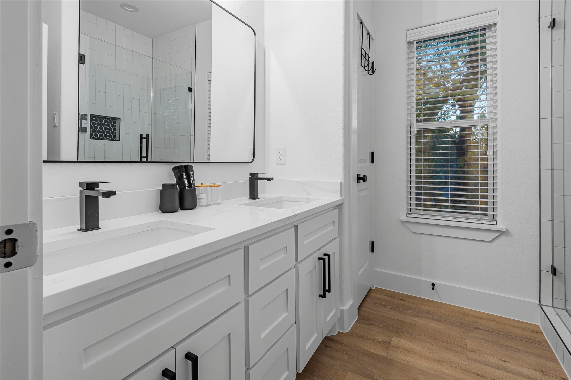 Elegant bathroom with a dual-sink vanity, sleek black fixtures, and a large mirror. Abundant natural light filters through the window, complementing the stylish tile shower.