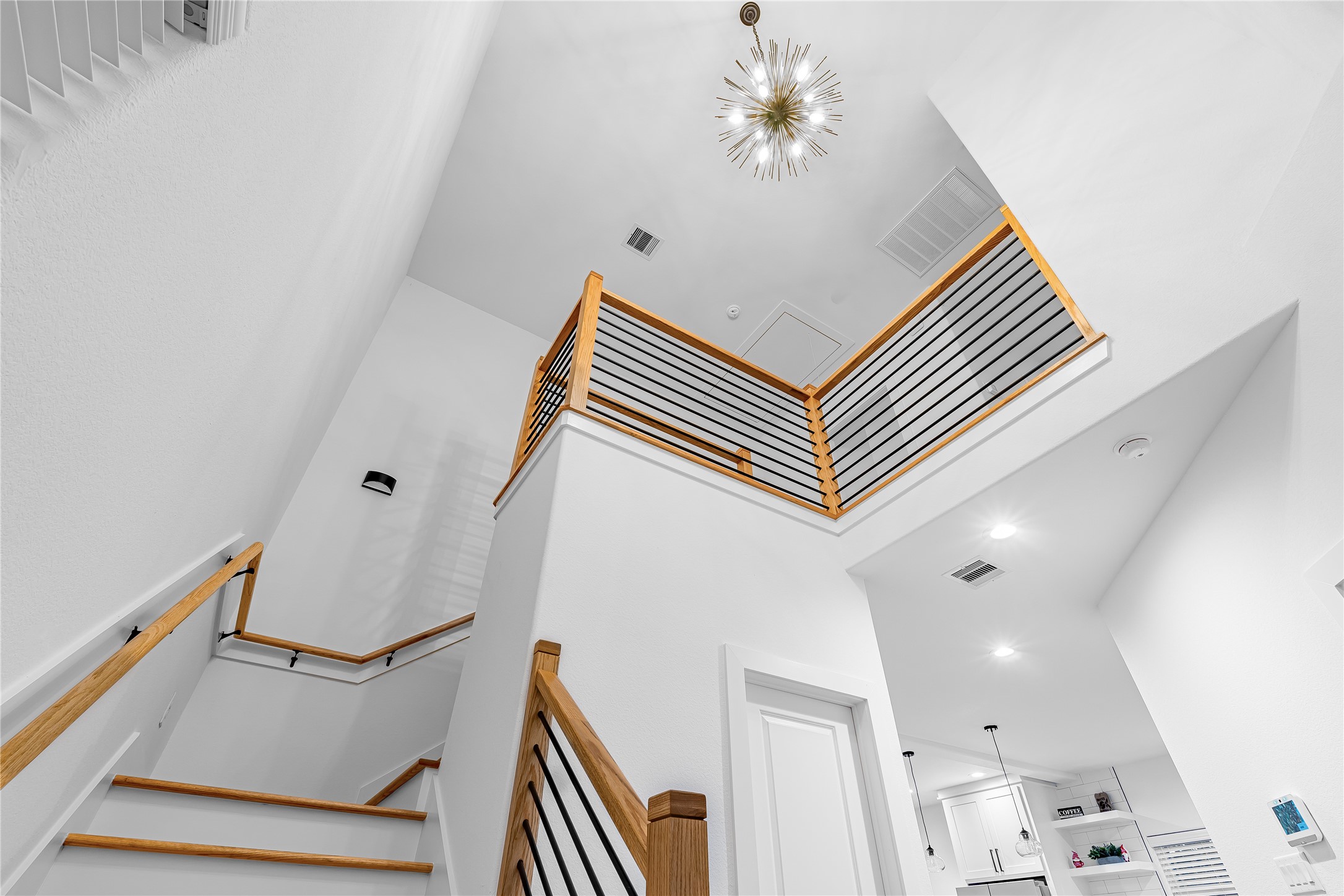 Stunning modern staircase with sleek wood and metal railings, highlighted by an elegant chandelier, leads to an airy upper level.