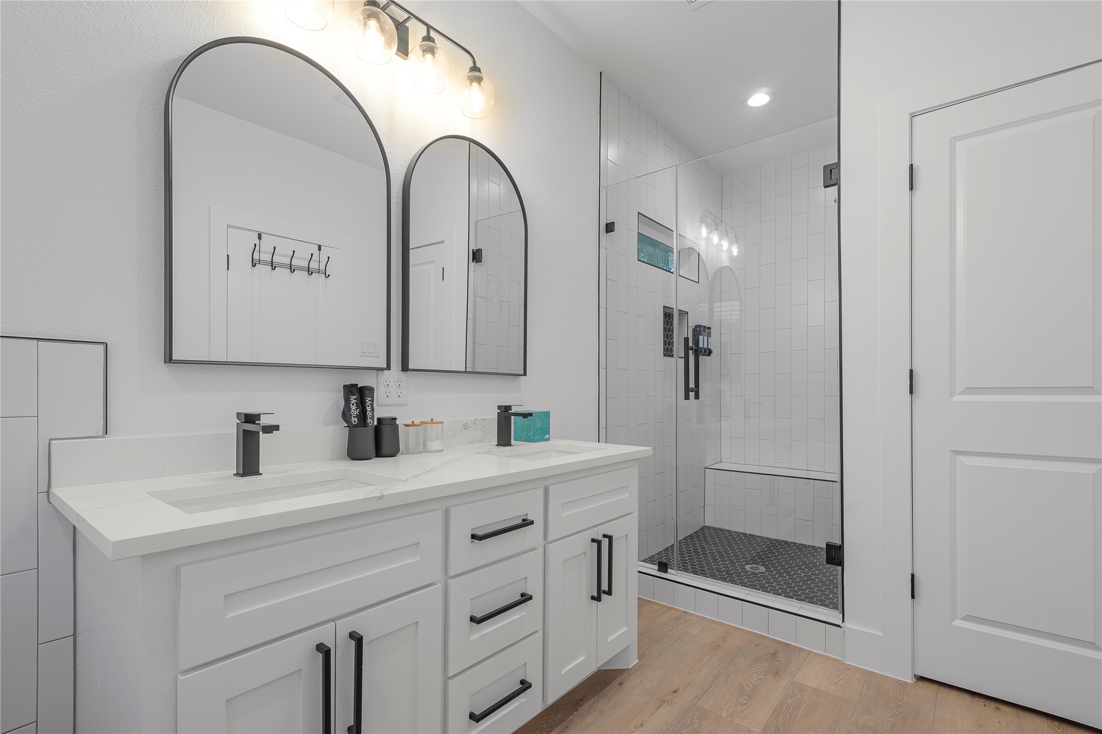 Sleek and modern bathroom featuring a double vanity with elegant arched mirrors, stylish black fixtures, and a spacious glass-enclosed shower with a built-in bench.