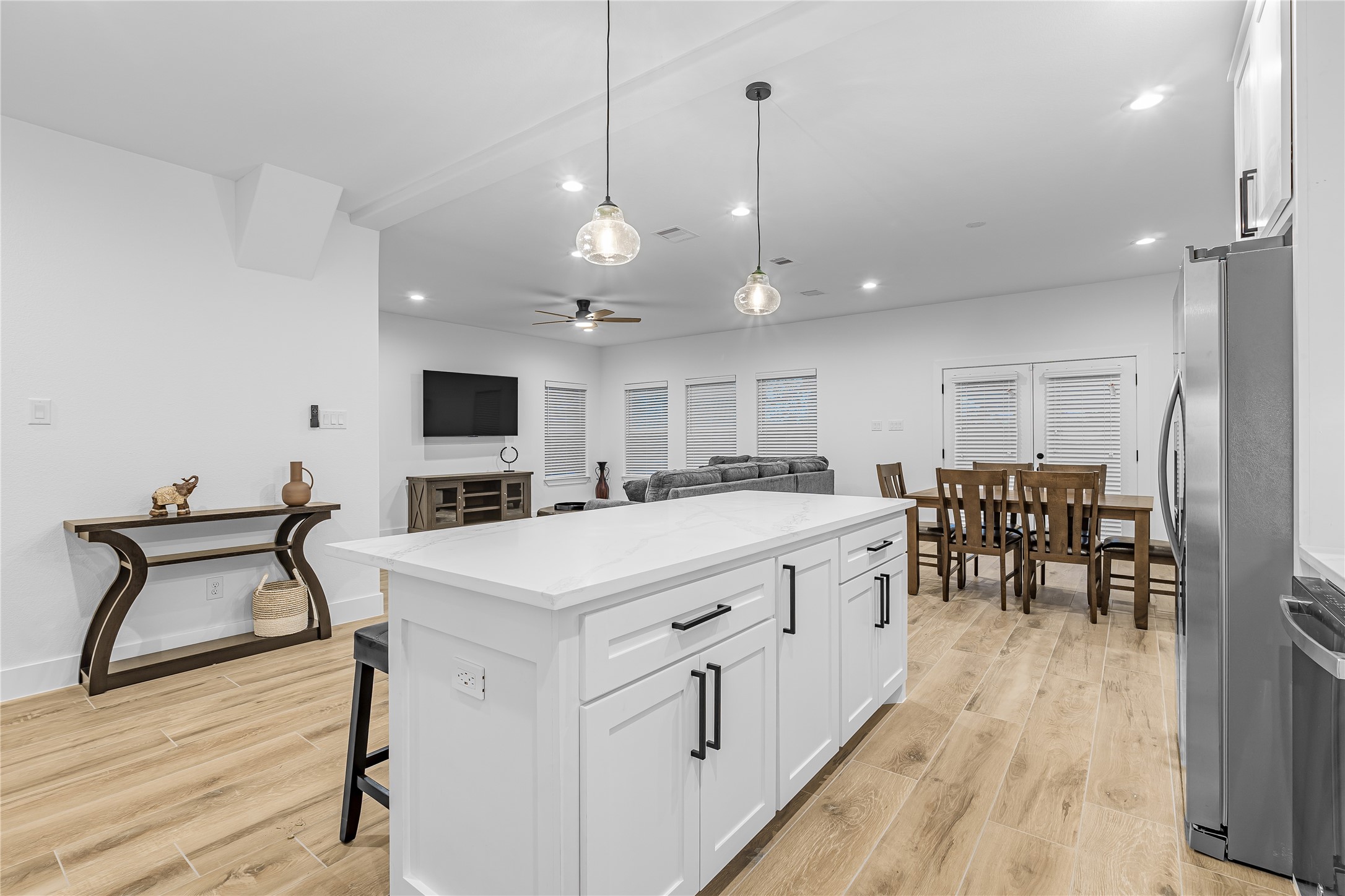 Open-concept living space with a modern kitchen island, elegant pendant lighting, and seamless flow to the dining and living areas. Actual furniture.