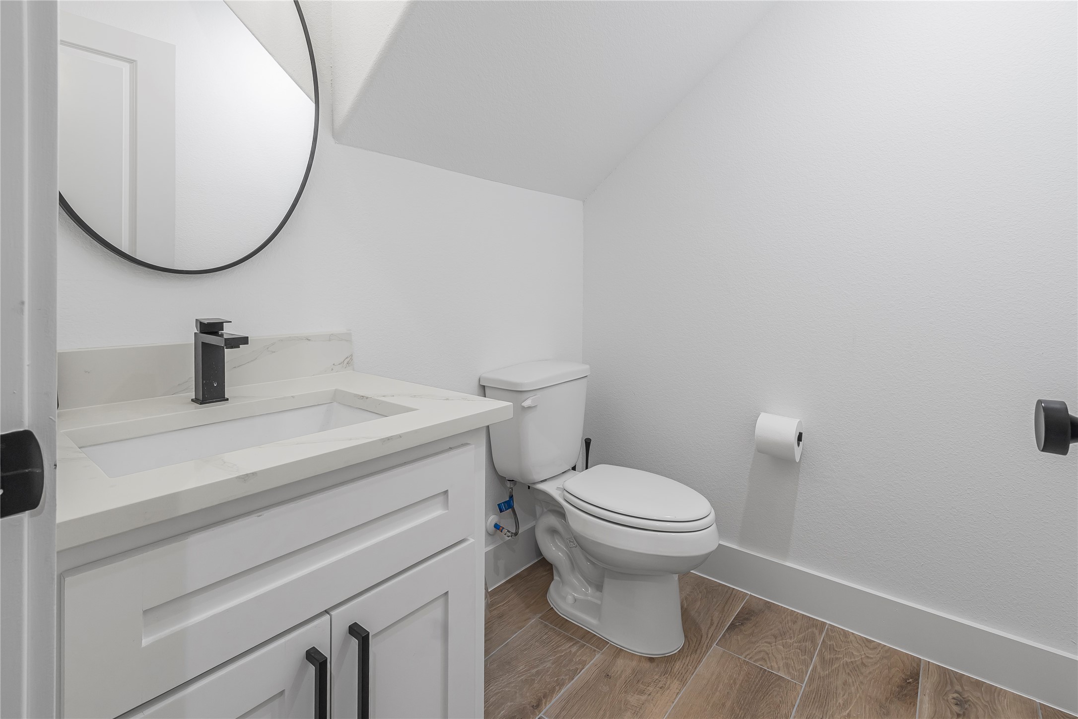 Chic powder room featuring a sleek white vanity with a quartz countertop, modern black fixtures, and warm wood-look flooring.