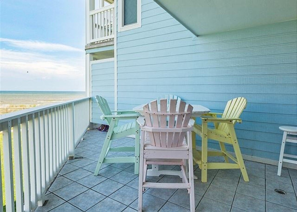 Charming oceanfront balcony with pastel Adirondack chairs, offering stunning sea views and a perfect spot for morning coffee or sunset relaxation.