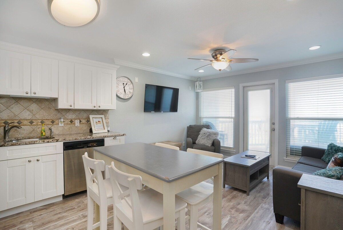 Bright and inviting open-concept living area featuring a modern kitchen with granite countertops, cozy seating, and ample natural light from large windows and patio door.
