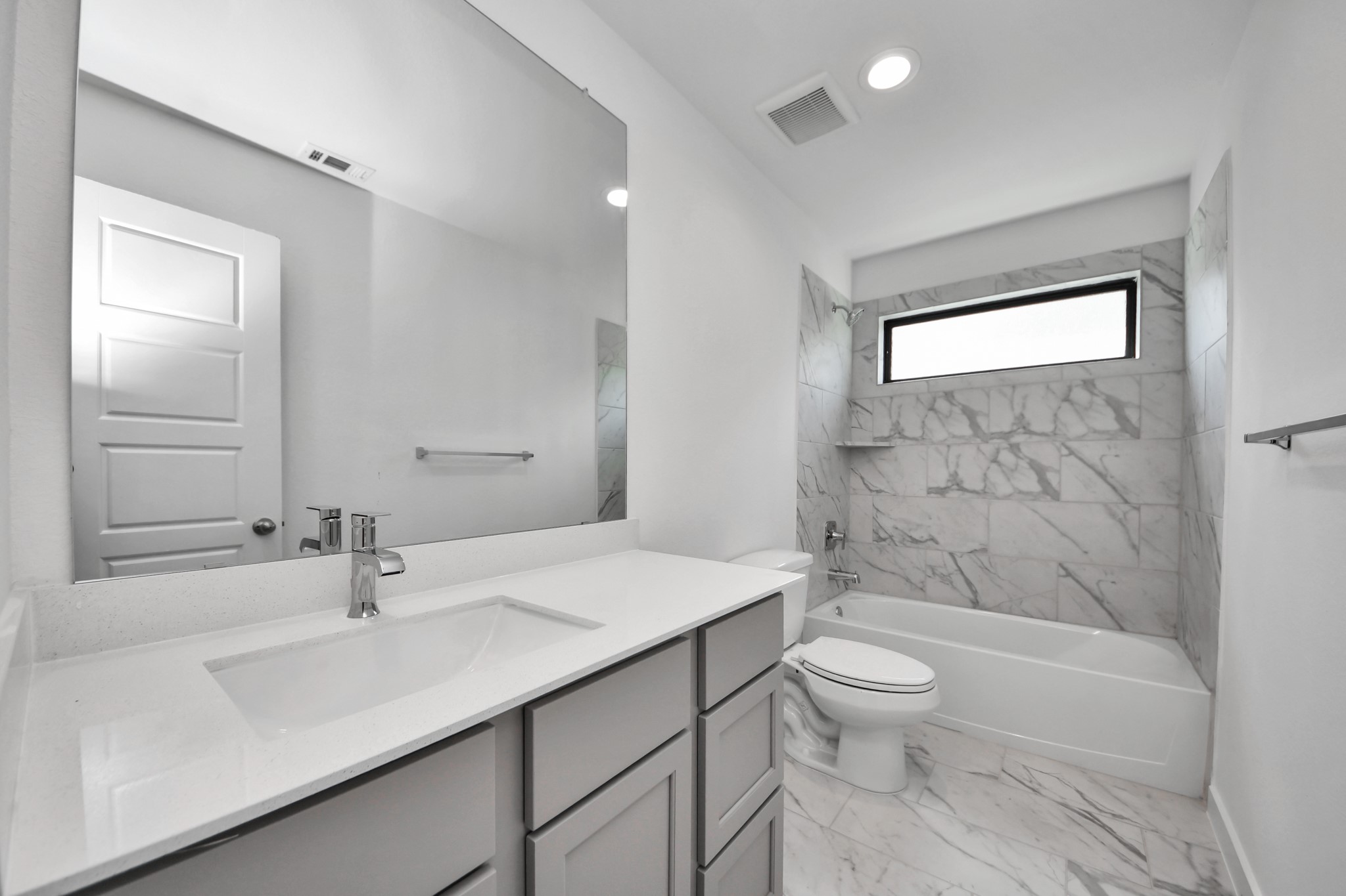 Secondary bath features tile flooring, bath/shower combo with tile surround, light stained wood cabinets, beautiful light countertop.