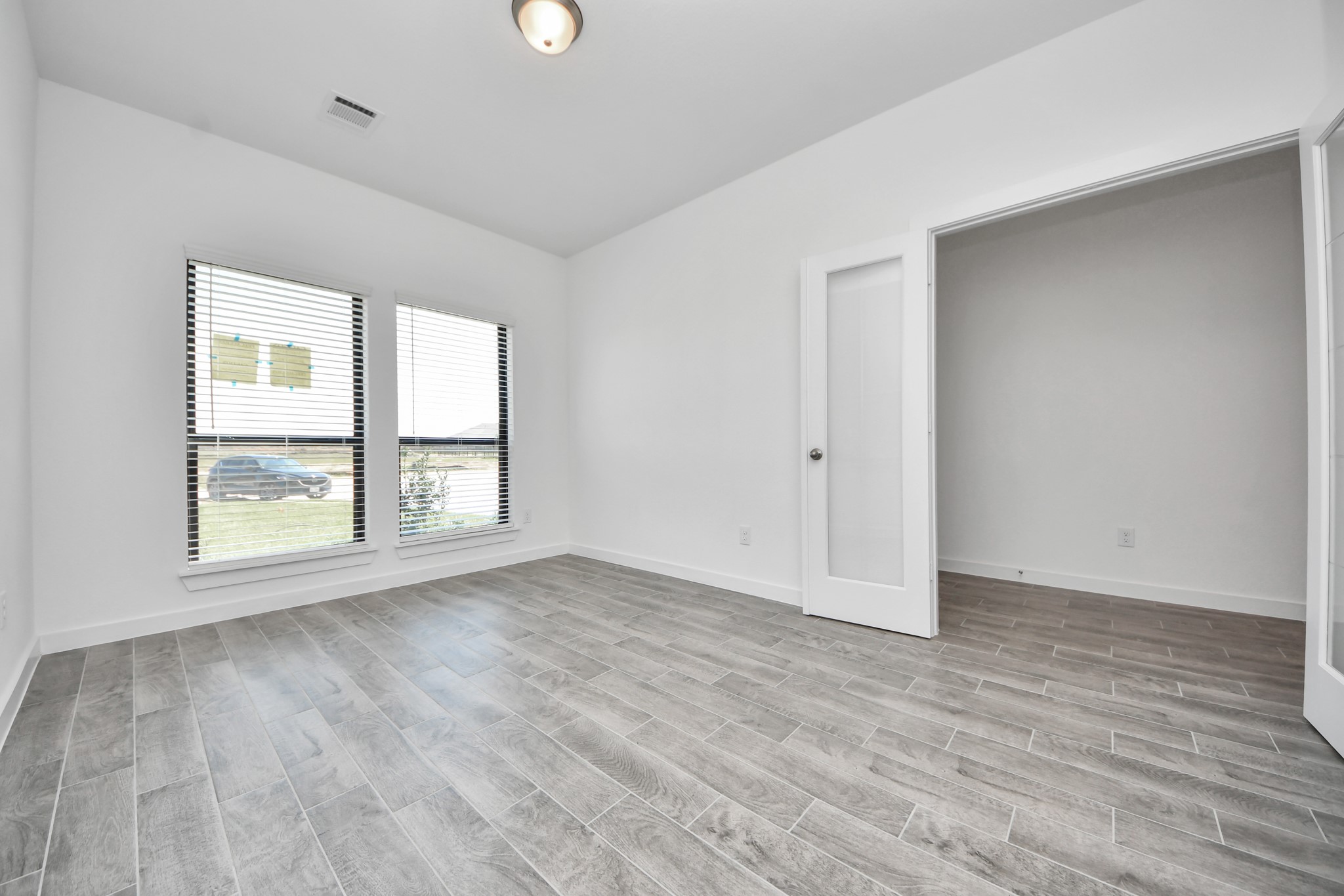 Experience the perfect blend of sophistication and warmth in this home office, boasting elegant wood-look tile flooring and flooded with natural light from expansive windows and French doors.