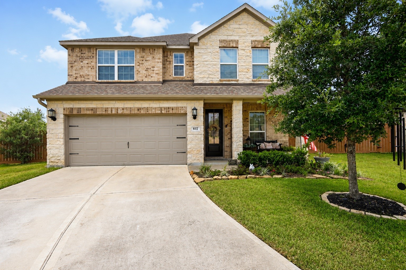 Charming two-story home with a welcoming brick and stone exterior, spacious two-car garage, and lush, well-maintained front yard.