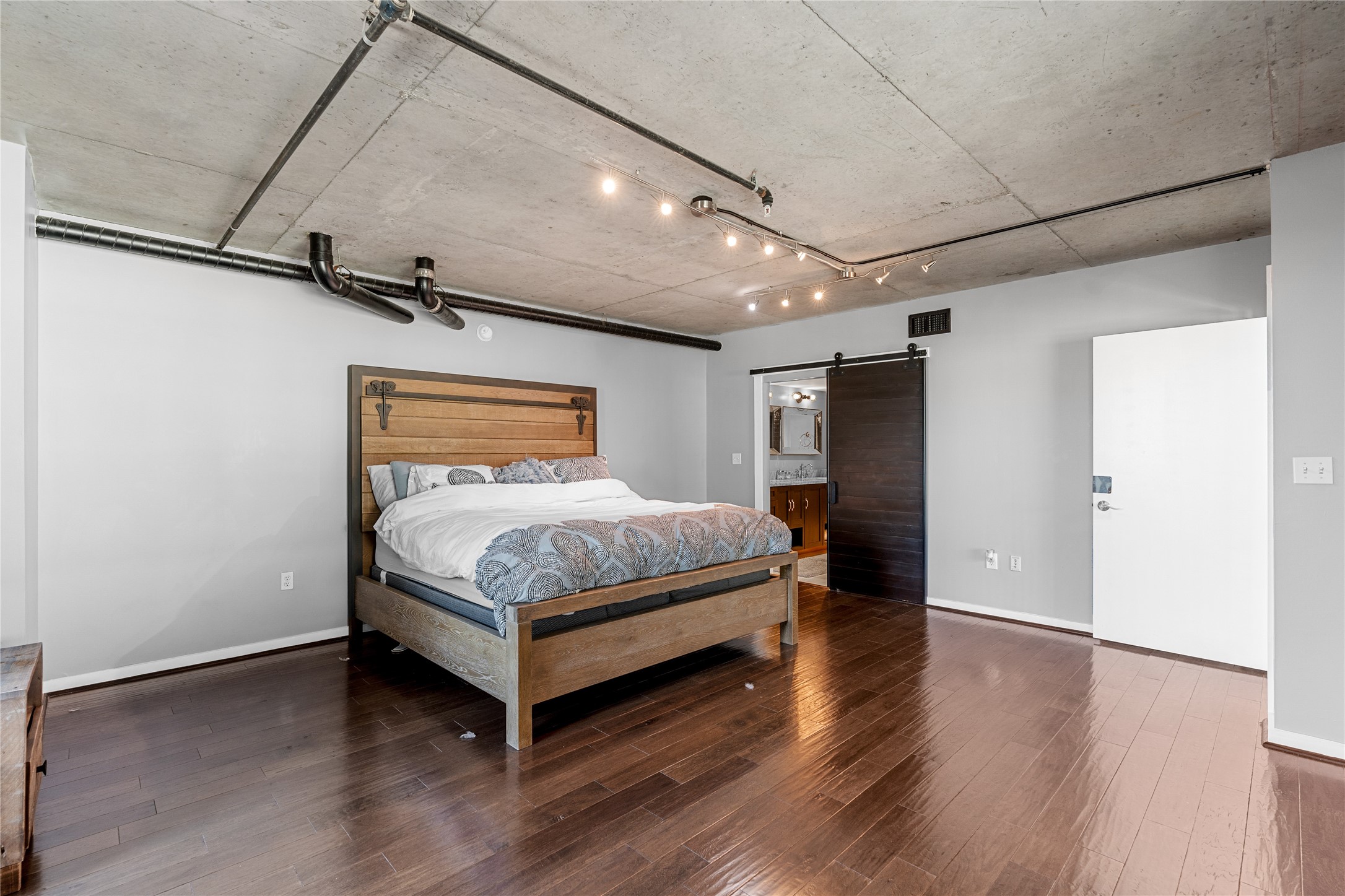 The spacious primary bedroom occupies the upper level, pairing warm wood flooring with exposed concrete ceilings for a refined take on the lofts industrial character.