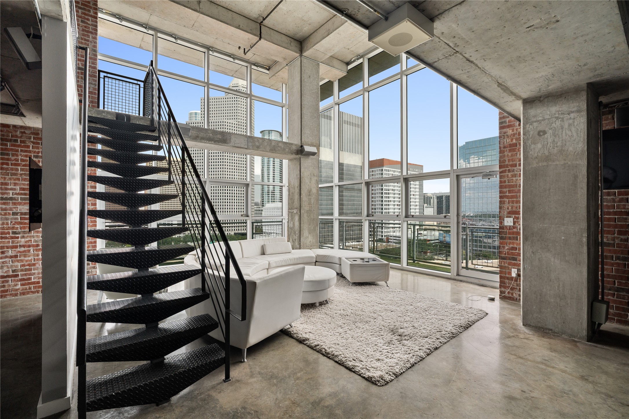 Soaring floor to ceiling windows flood the two story living area with natural light, while the open metal staircase reinforces the lofts dramatic industrial character.
