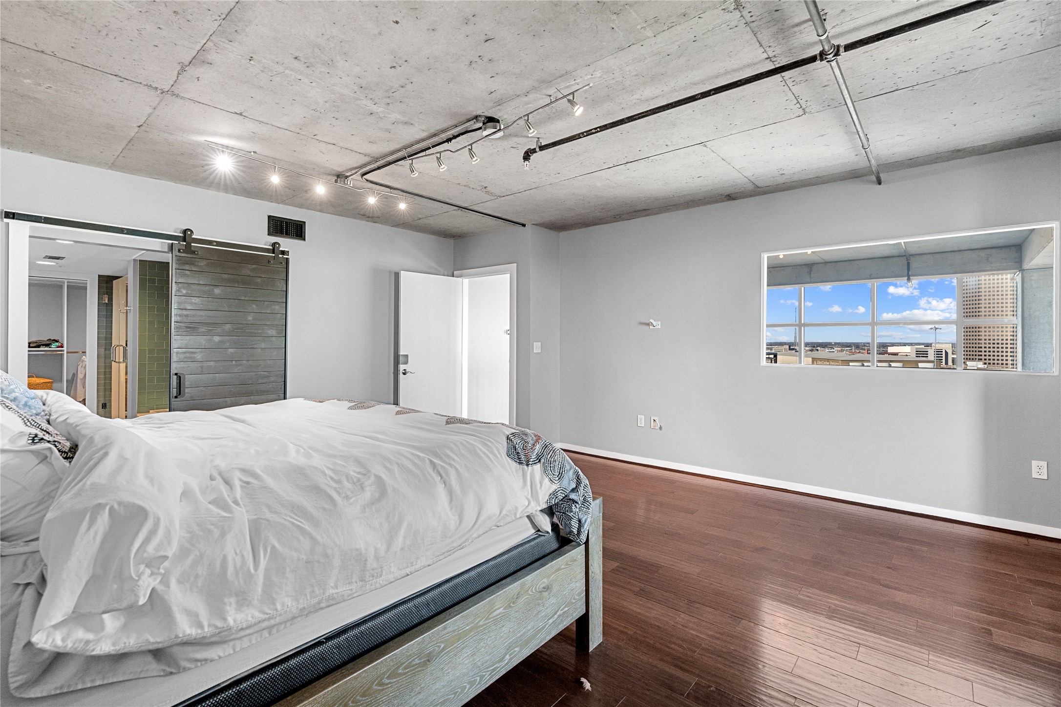 The primary suite continues the lofts industrial aesthetic with exposed concrete ceilings and warm wood floors, while a wide picture window brings natural light into the private retreat.