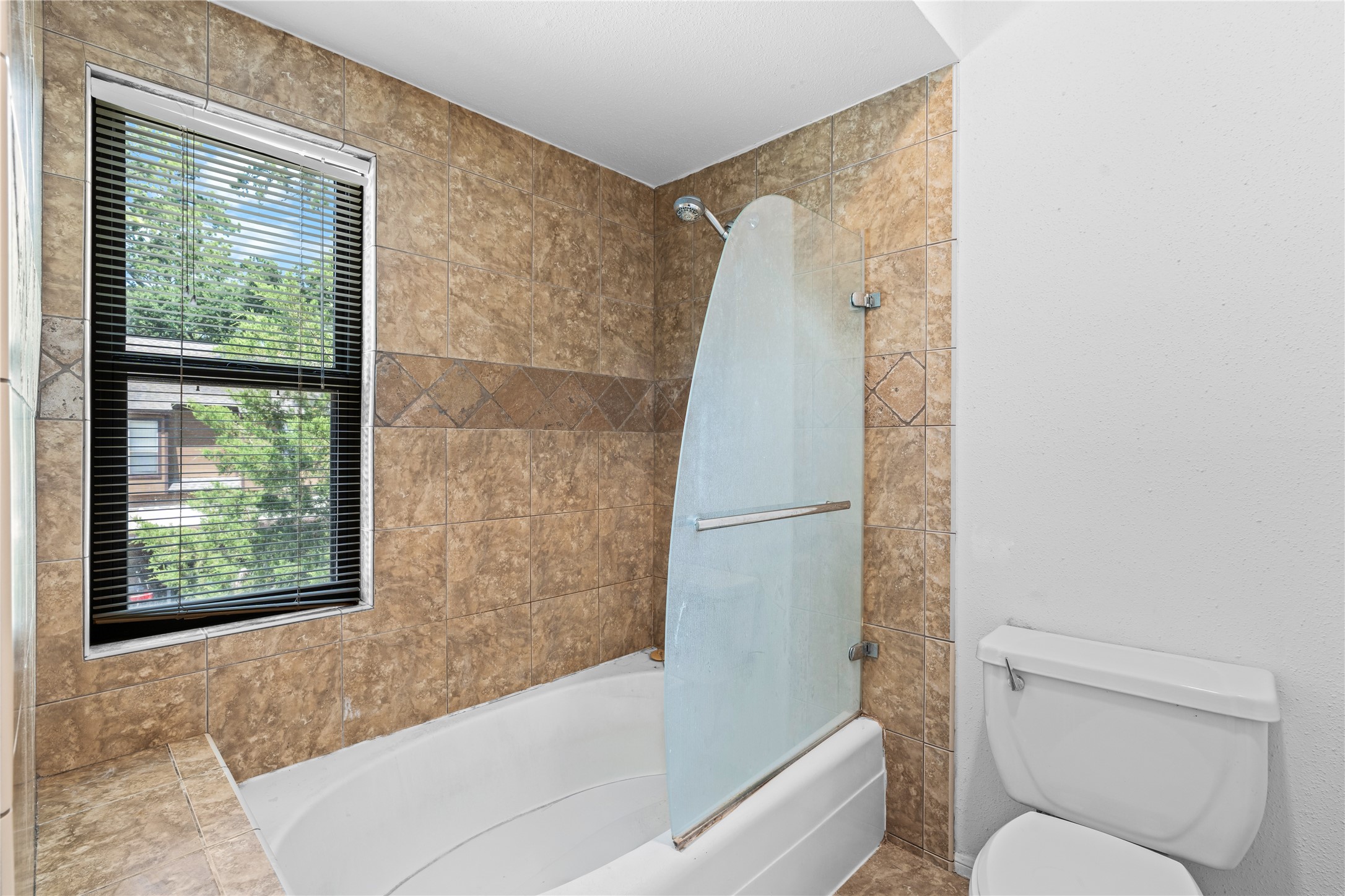 The primary bath features a fully tiled tub and shower surround, complemented by natural light from a nearby window.