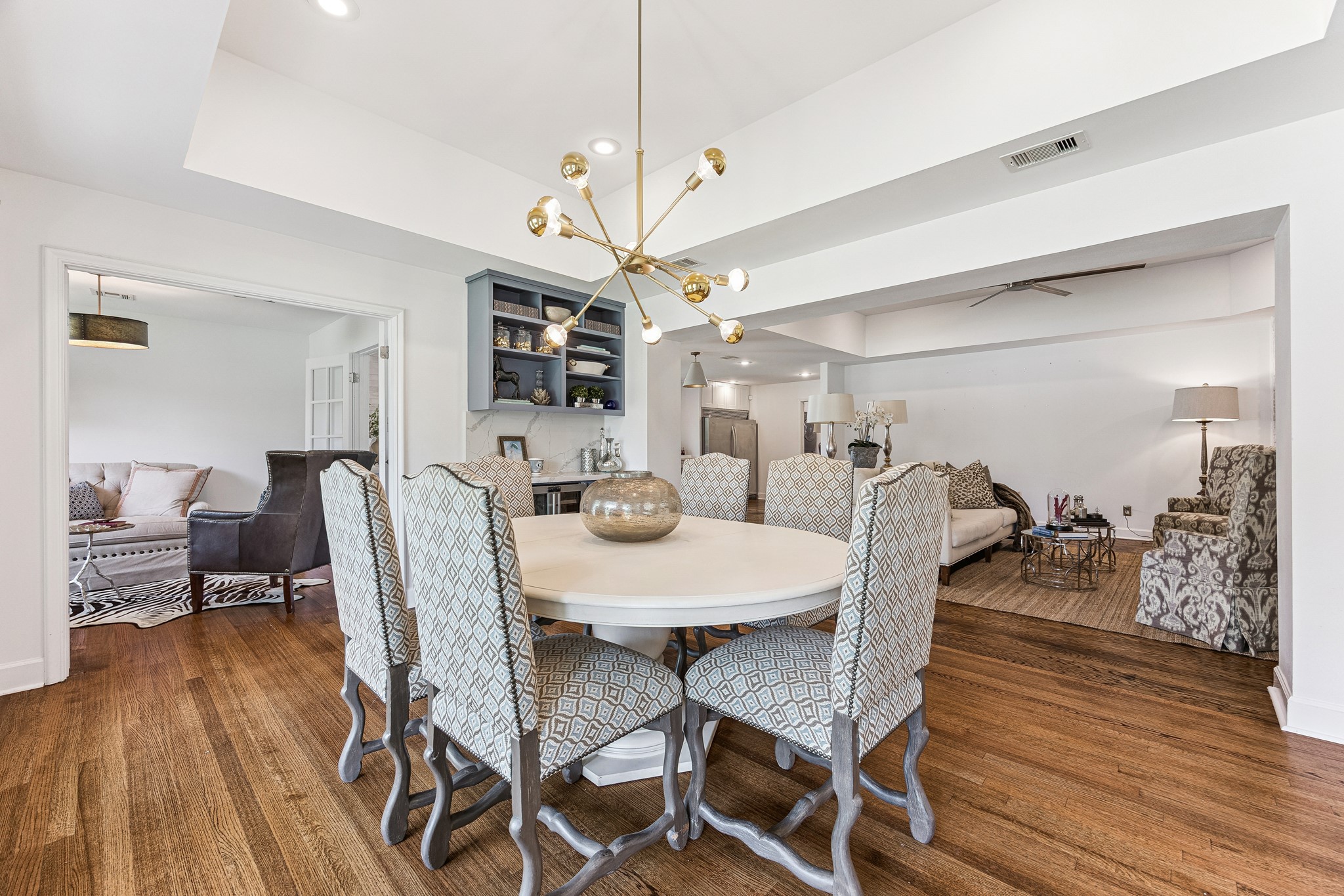 The formal dining room (15x12) is anchored by a
striking brass chandelier and warm hardwood floors beneath a tray ceiling. Abundant natural light fills the space through windows with blinds, creating a
bright and inviting setting for both everyday meals and formal gatherings. The adjacent dry bar adds a refined touch and convenient serving space, making the room especially well suited for entertaining.
