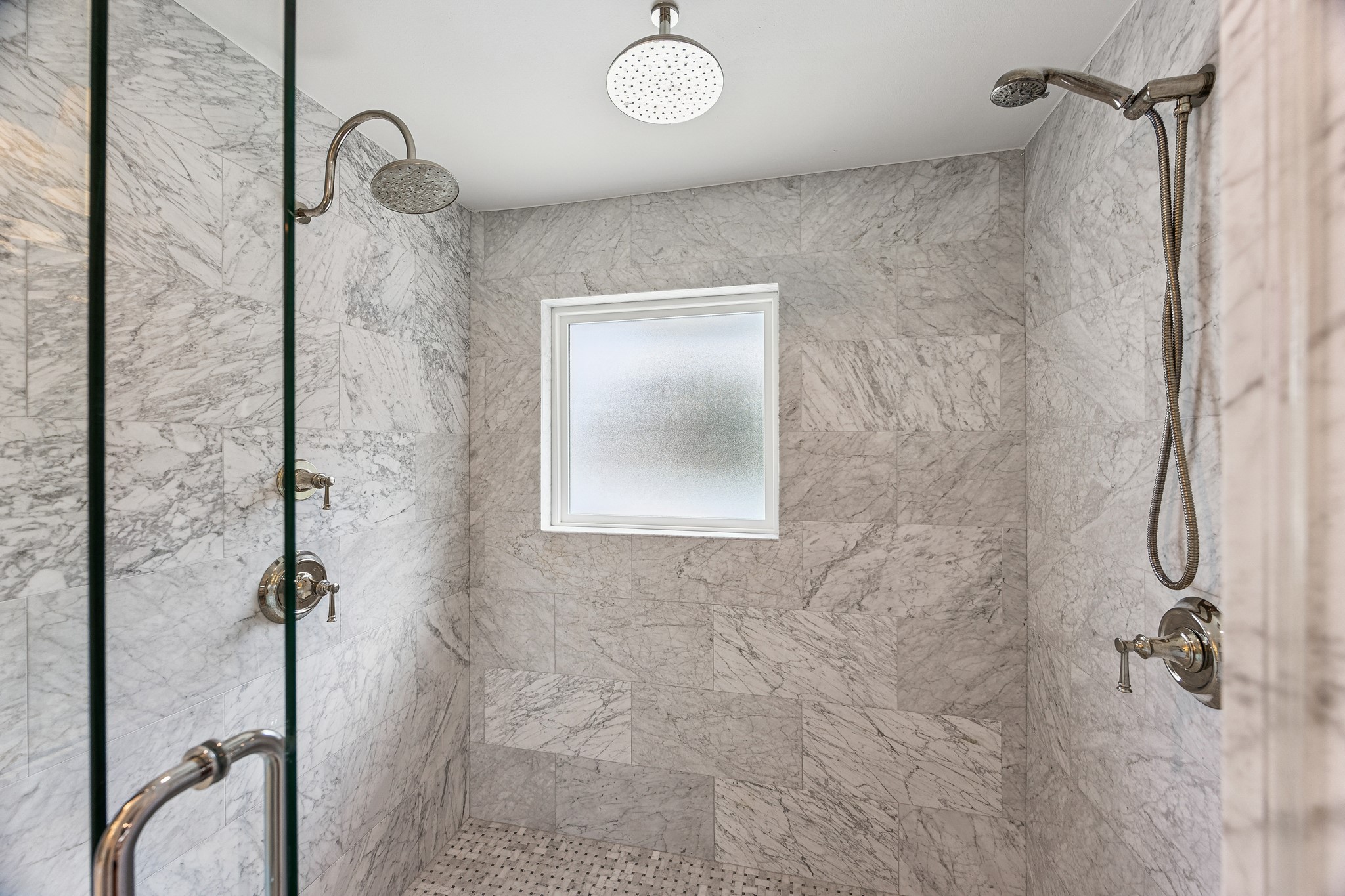 The beautifully updated primary bathroom features an oversized walk-in shower with marble-look tile and a frameless glass enclosure. Dual showerheads and a built-in bench create a luxurious, spa-inspired experience.