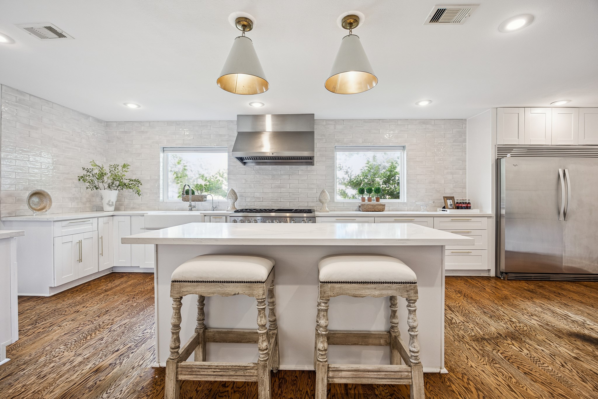 (25x10) The breakfast island kitchen is illuminated with designer pendant lighting, casting a warm glow across the custom cabinetry. Professional stainless steel appliances and custom tile backsplash enhance this space. Every detail has been curated to elevate the everyday culinary experience.