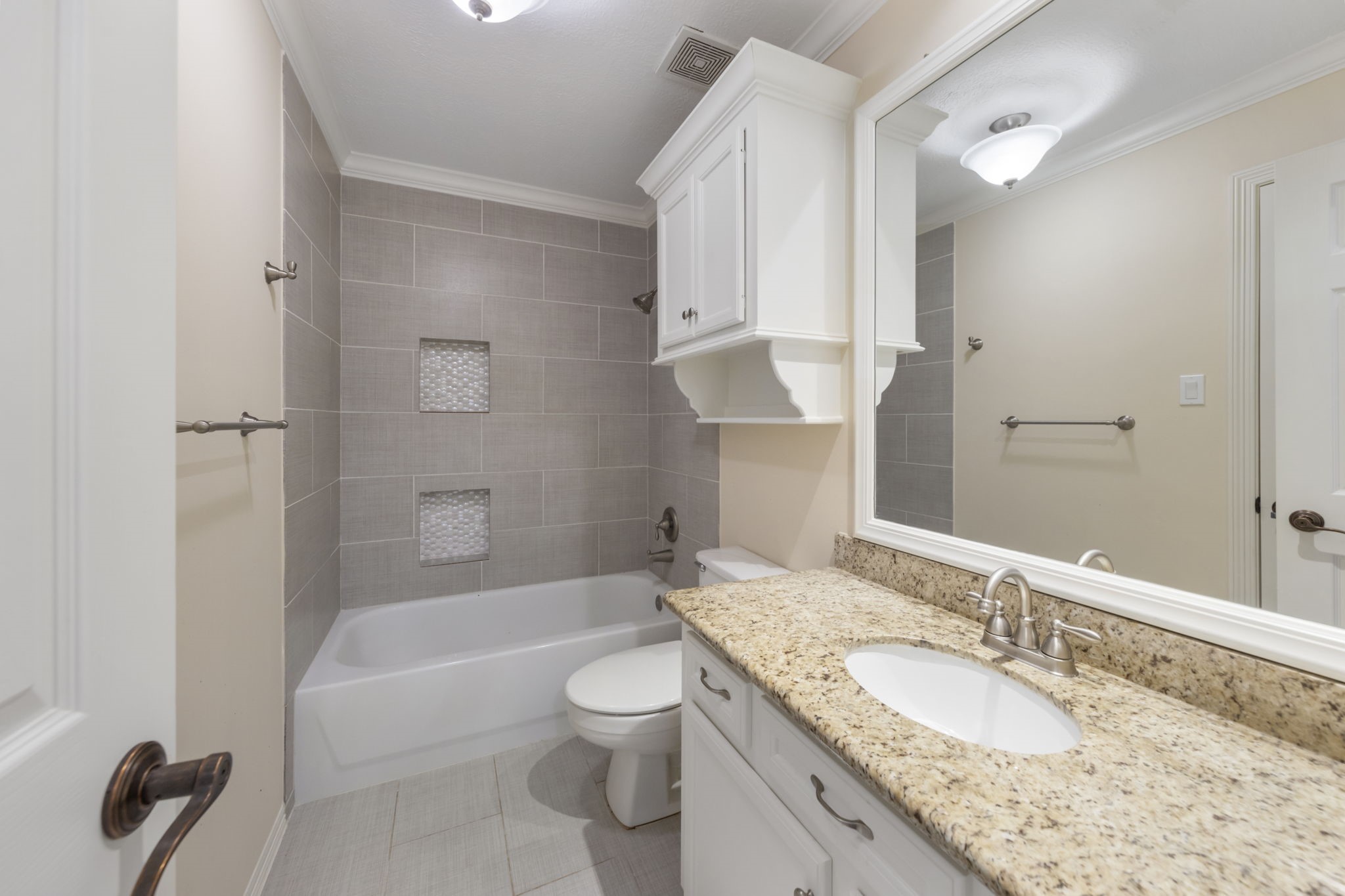 This bathroom, located at the top of the back stairs, offers ensuite access from the bedroom and hallway access for guests. It features updated tile, a tub/shower combo, and granite countertops.