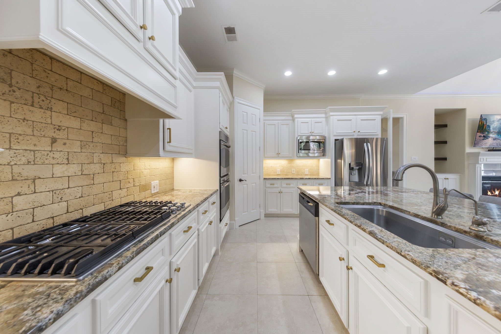 The chefs kitchen features a gas cooktop, stainless steel appliances, light cabinetry, and a large stainless steel sink set in a spacious island.