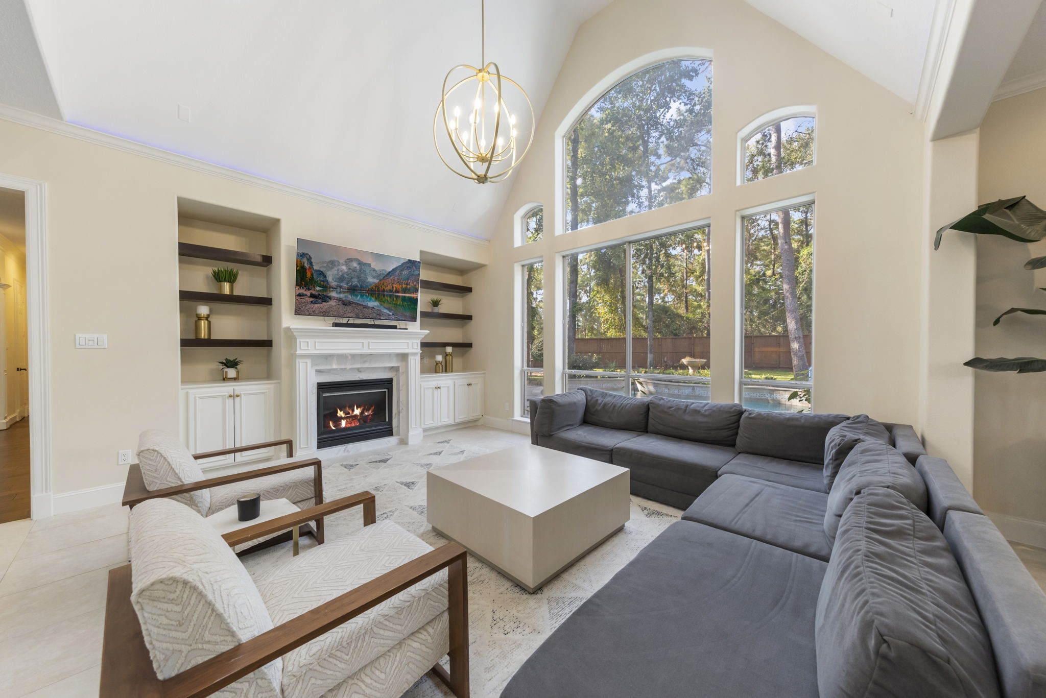 The family room boasts soaring ceilings, a large window with views of the backyard retreat, stylish pendant lighting, and built-ins that frame a cozy gas log fireplace.