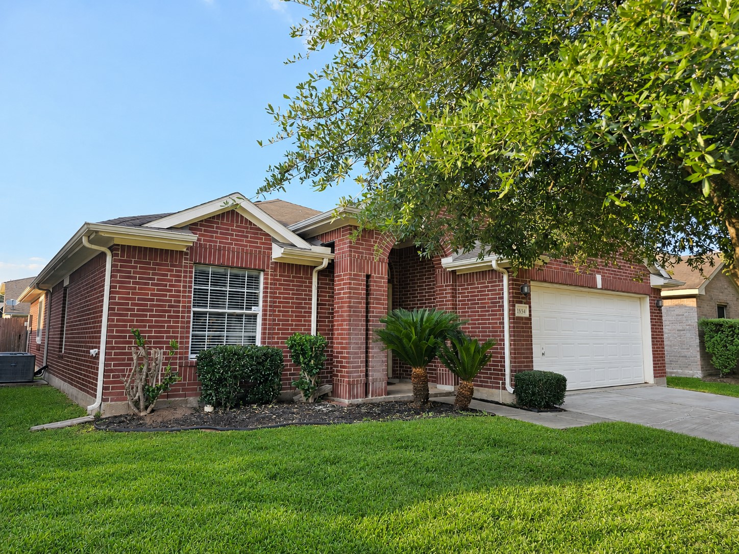 Charming brick home with a welcoming front porch, well-maintained landscaping, and a spacious two-car garage.