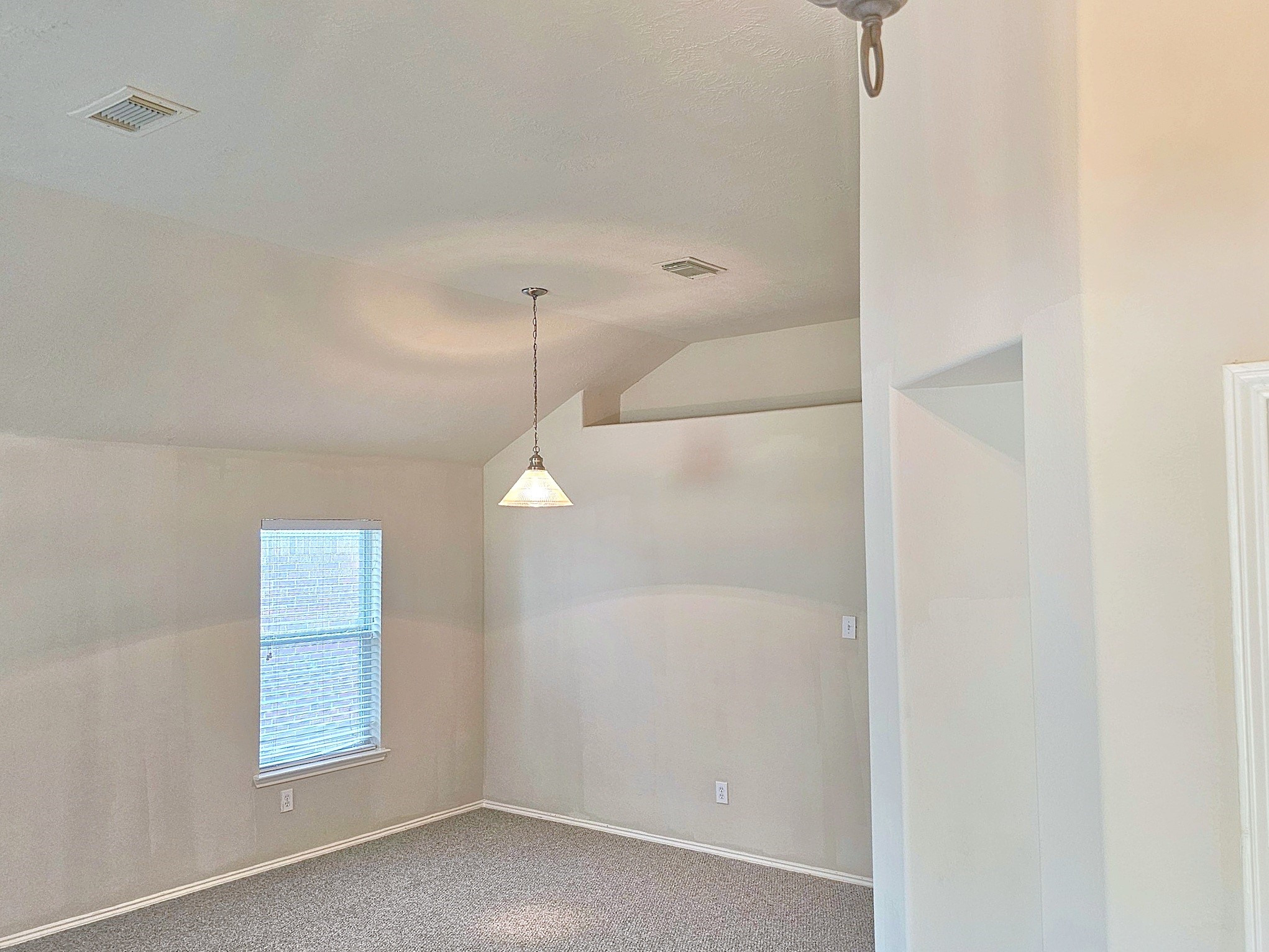 Bright room with vaulted ceilings, soft carpet flooring, and a large window providing ample natural light.
