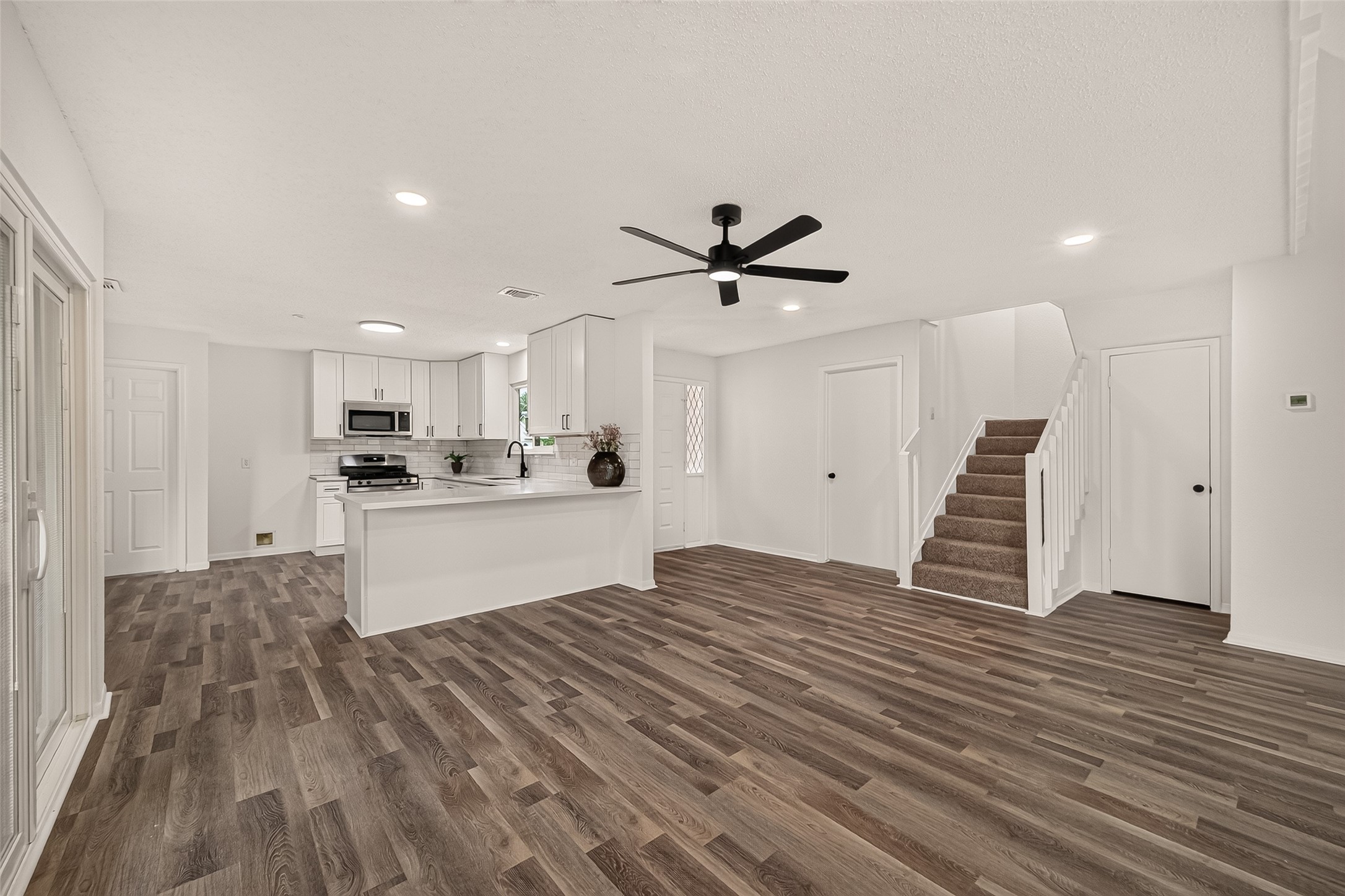Open-concept living area with sleek luxury vinyl plank floors, modern ceiling fan, and a bright kitchen featuring stainless steel appliances and an inviting breakfast bar.