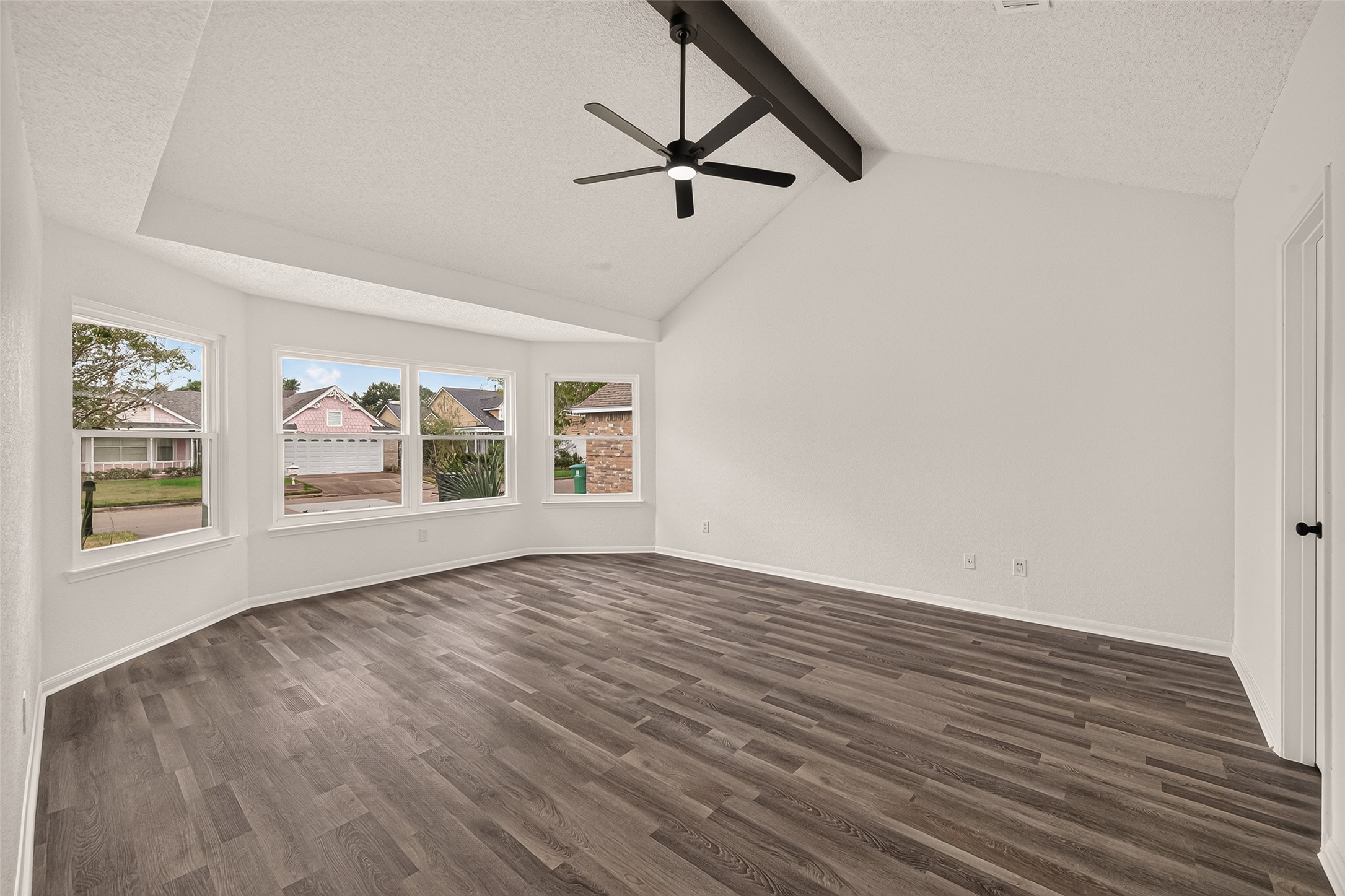 Spacious primary bedroom with vaulted ceilings, exposed beams and large windows for ample natural light