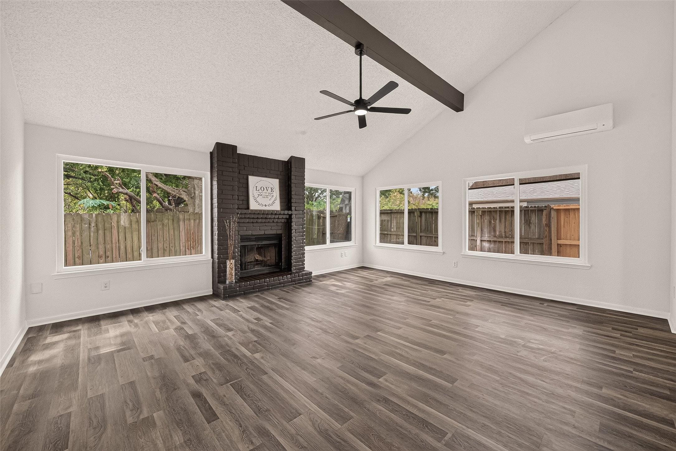 Spacious living room with vaulted ceilings, featuring a sleek dark brown brick fireplace, and abundant natural light from large windows.