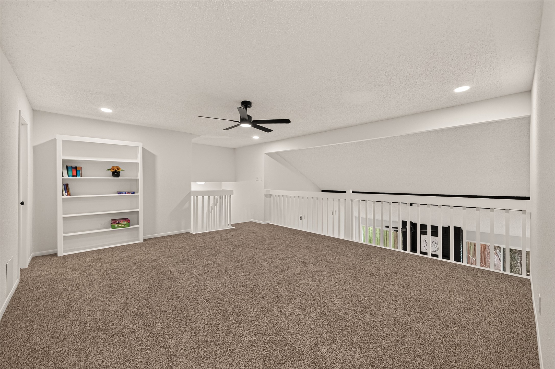 Spacious game-room with plush new carpeting, built-in shelving, and a modern ceiling fan, ideal for a cozy living space or home office.
