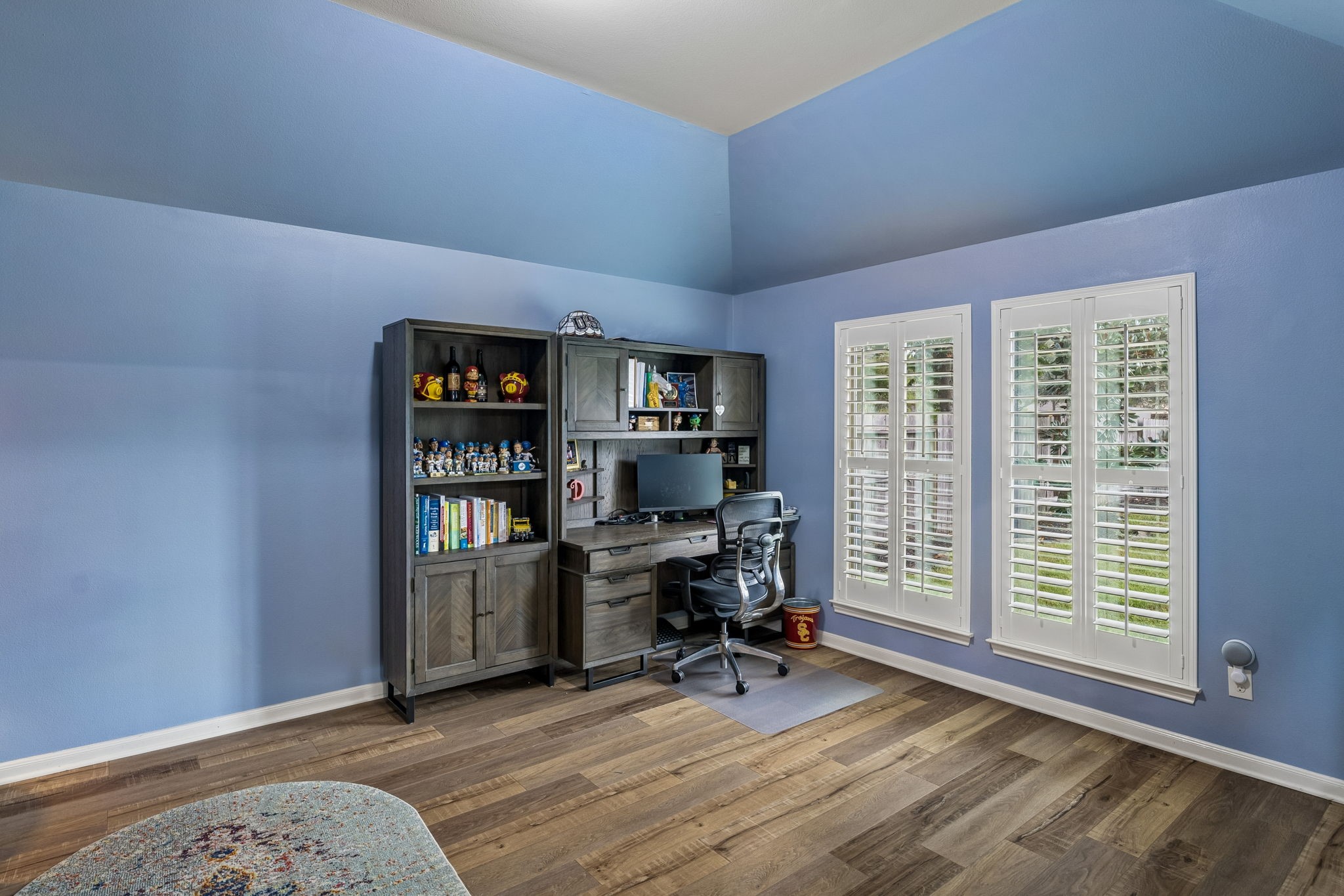 Versatile room with built-in shelving, wood flooring, and multiple windows providing natural light.
