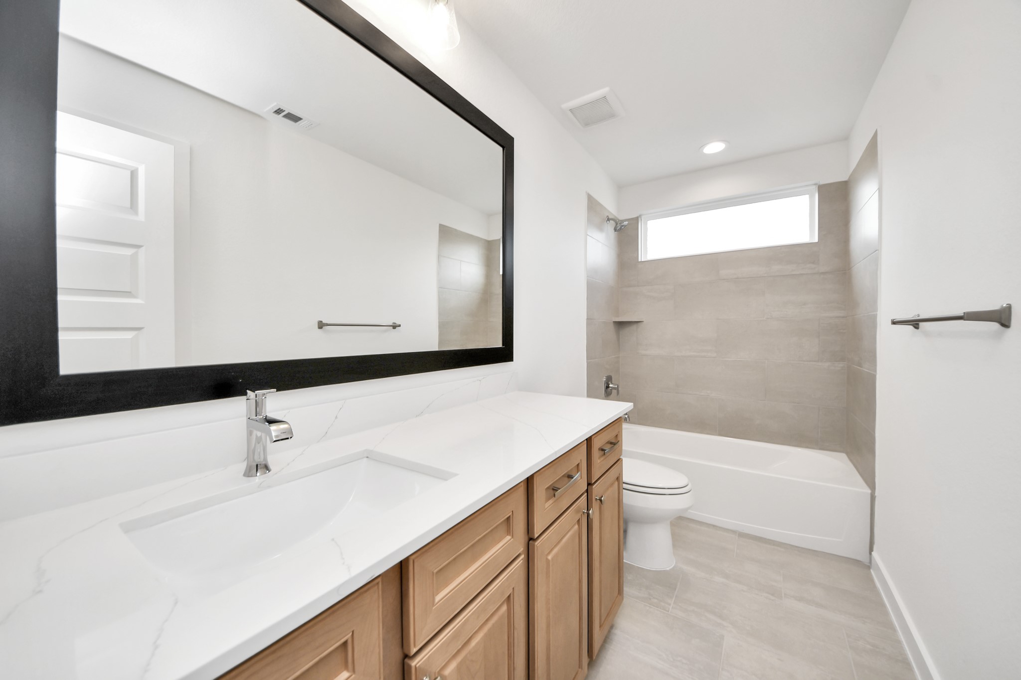 Secondary bath features tile flooring, bath/shower combo with tile surround, light stained wood cabinets, beautiful light countertop. Sample photo of completed home with similar floor plan. Actual colors and selections may vary.