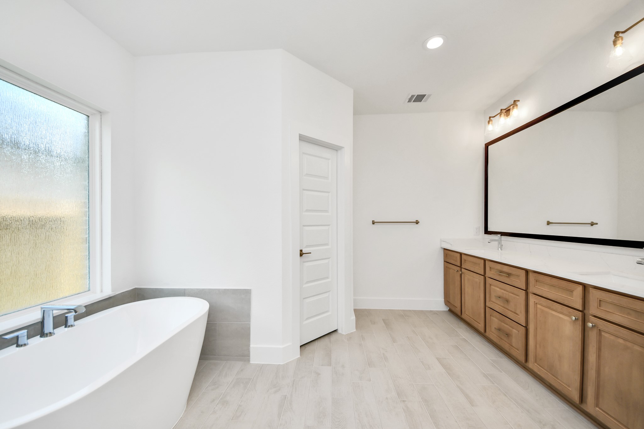 Escape to a spa-like oasis in this primary bathroom. Enjoy a walk-in shower with tile surround, a separate garden tub with custom detailing, and an elegant vanity featuring light countertops, modern hardware, and beautiful vanity lights. Experience luxury and relaxation in every detail. Sample photo of completed home with similar floor plan. Actual colors and selections may vary.