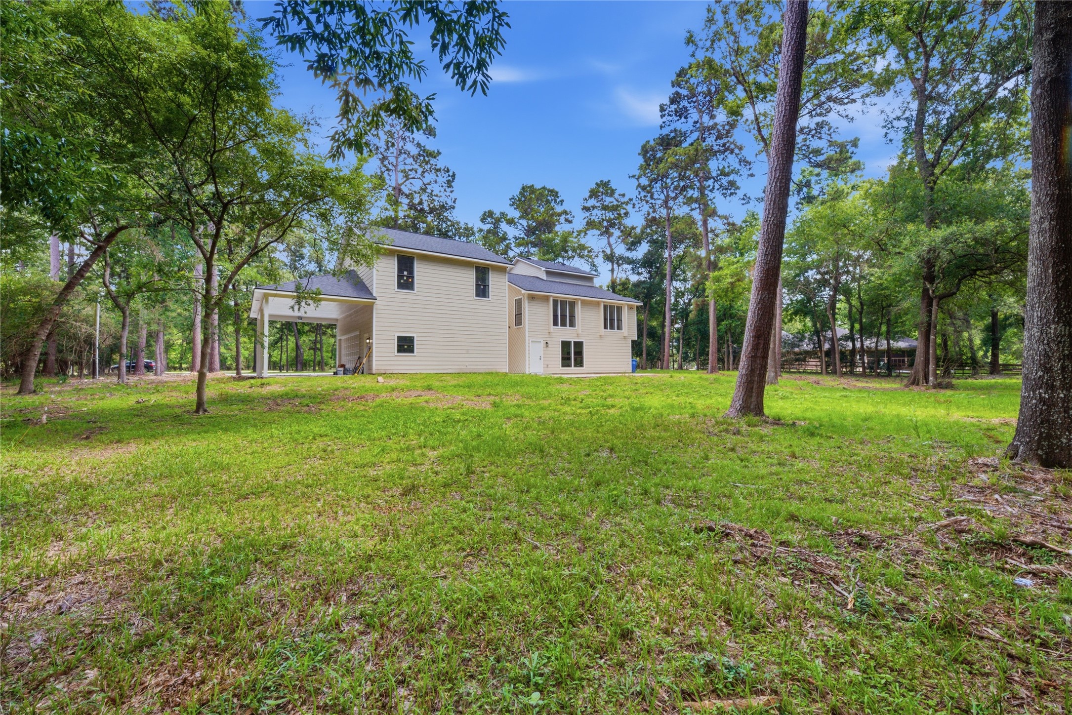 Side view showing the relationship between the main home and detached garage structure, both nestled within the mature treeline. Generous side yard ideal for entertaining, gardening, or equestrian use.