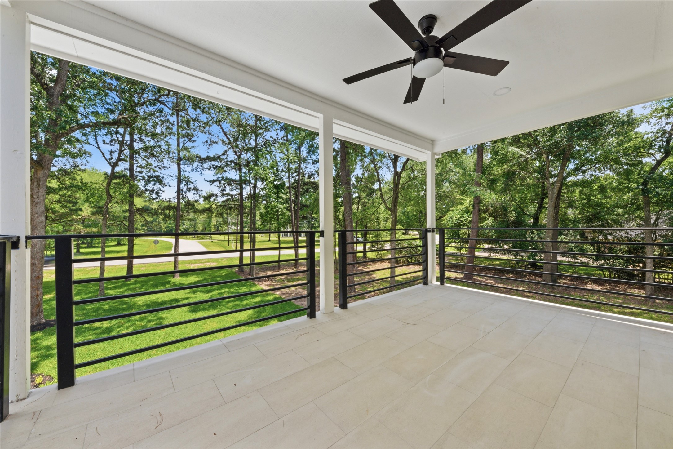 Generous covered upper balcony off the 3rd-floor second primary suite. Features designer ceiling fan, horizontal black metal railing, tiled flooring, and serene treetop views of the wooded 1.67-acre lot. Perfect for morning coffee or evening sunsets.
