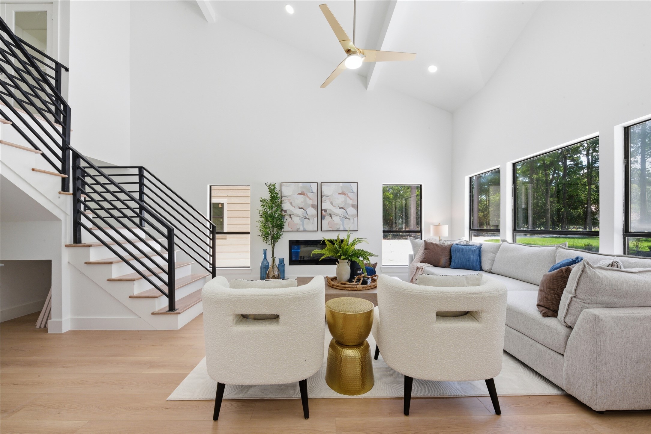 Soaring 20-ft ceilings, floating steel staircase with white oak treads and horizontal black metal rail, linear electric fireplace, and walls of windows overlooking the wooded acreage. Wide- luxury vinyl plank  floors throughout.