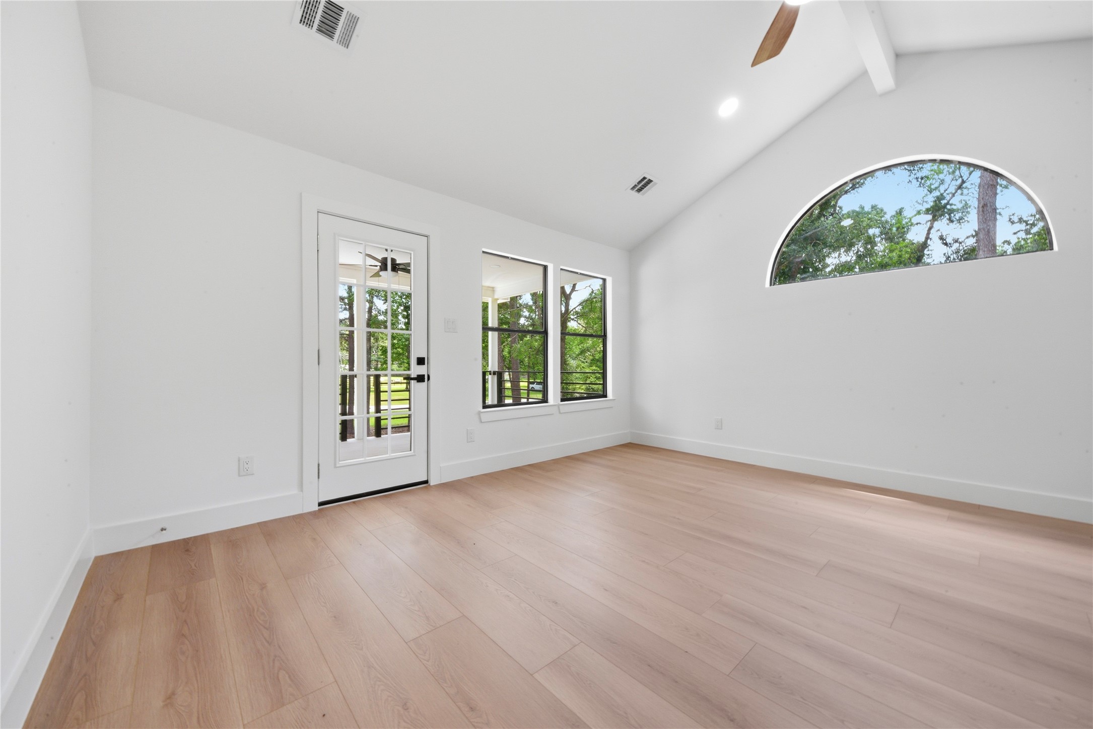 Stunning third-floor second primary suite featuring vaulted ceiling with exposed beam, designer ceiling fan, half-moon accent window, and private door access to a covered balcony overlooking the treeline.
