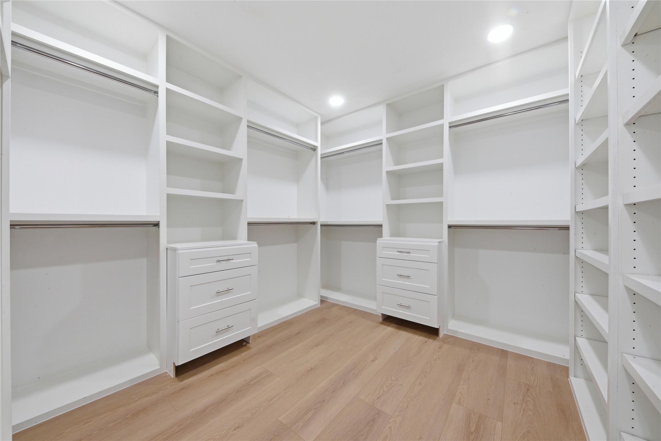 Boutique-style primary walk-in closet featuring built-in shaker drawers, double hanging rods, adjustable shelving, custom shoe wall, and wide-plank floors. Designed for serious storage and daily luxury.