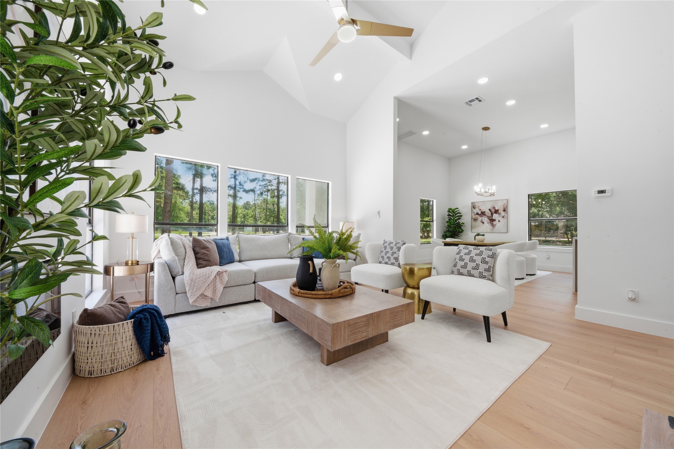 Open-concept flow from living room to dining area and kitchen beyond. Statement chandelier visible in dining nook, soaring vaulted ceilings, and seamless sight lines make this layout perfect for entertaining.