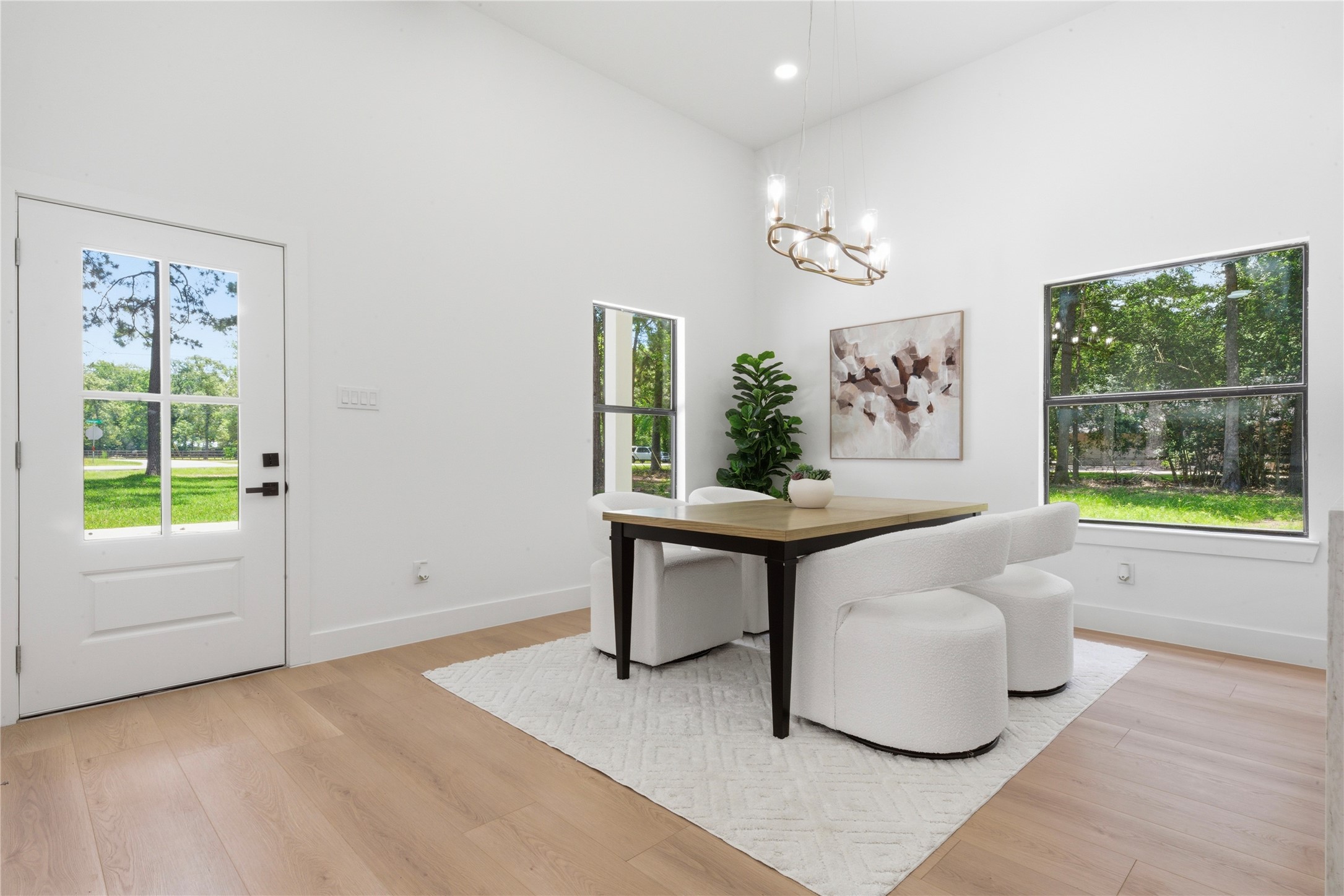 Bright dining area with statement chandelier, designer lighting, and gorgeous natural light from the front entry. Wide-plank luxury vinyl floors and clean modern lines create an elevated everyday dining experience.