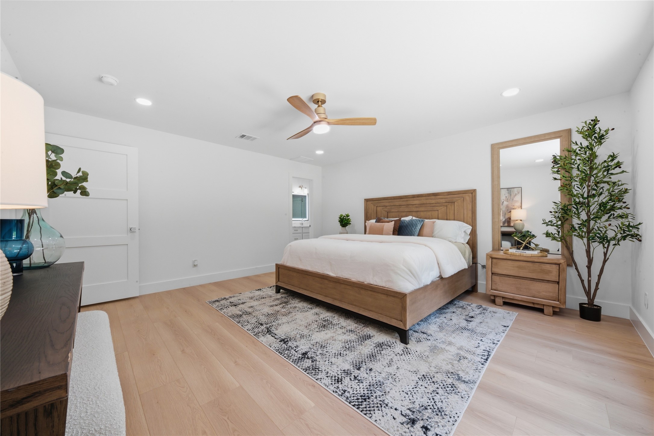 First-floor primary suite showing access to the ensuite spa bath and oversized footprint. Standard ceiling, designer fan, and natural light pour into this main-level retreat.