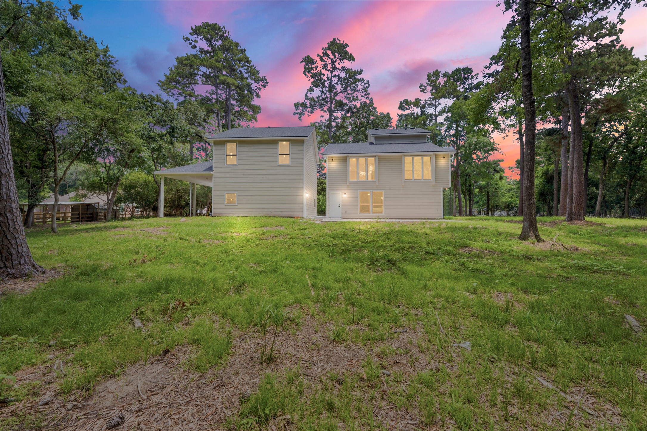 Magical twilight view of the rear elevation of the main home, glowing windows showcasing the great room and second primary suite. Set on 1.67 wooded acres in coveted Cimarron Country. Mature pines and natural privacy frame the property.