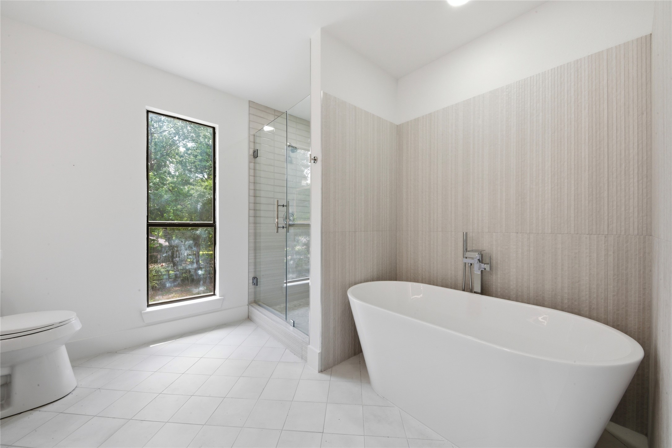 Spa-style retreat featuring a deep freestanding soaking tub, hand-held tub filler, and oversized frameless glass shower with floor-to-ceiling vertical tile. A true sanctuary for the second primary suite.