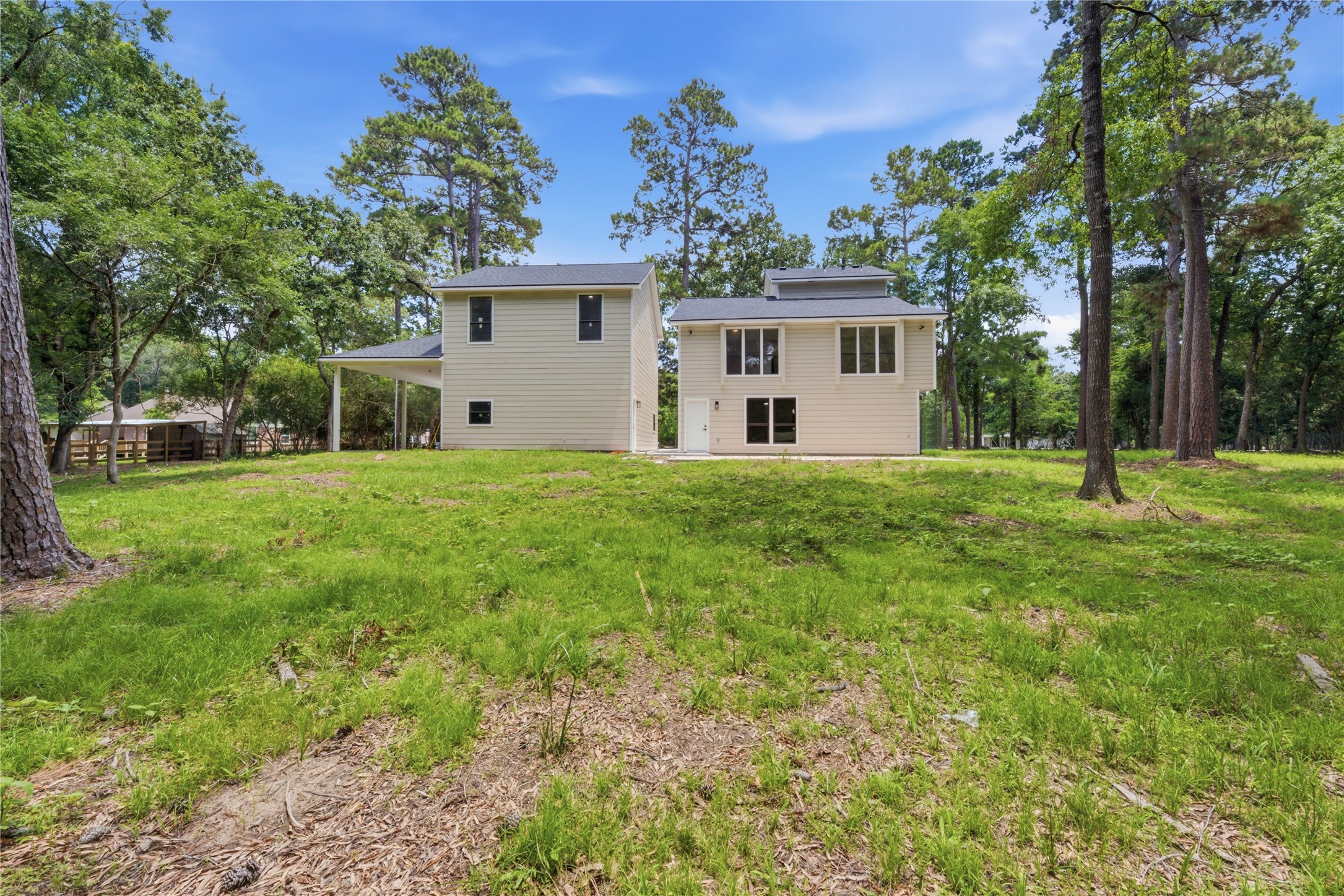 Daytime view of the rear elevation showcasing the home's substantial profile, modern board-and-batten siding, and the scale of the surrounding wooded lot. AC units neatly tucked at the side.