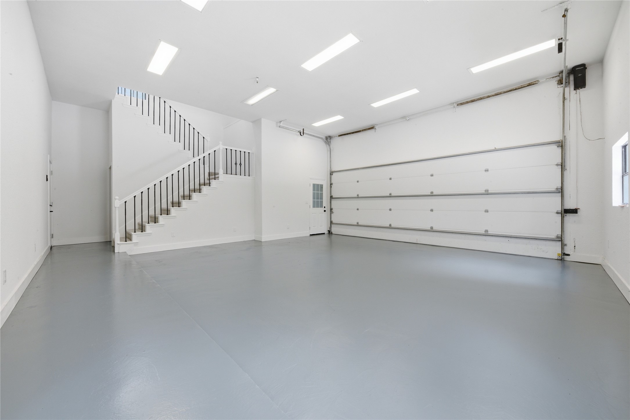 Massive, detached structure ground floor featuring oversized garage door, iron-railed staircase to the upper suite, vaulted ceiling with skylights, and side door access. Currently configured as a garage but functions as flexible workshop, gym, studio, or vehicle storage.